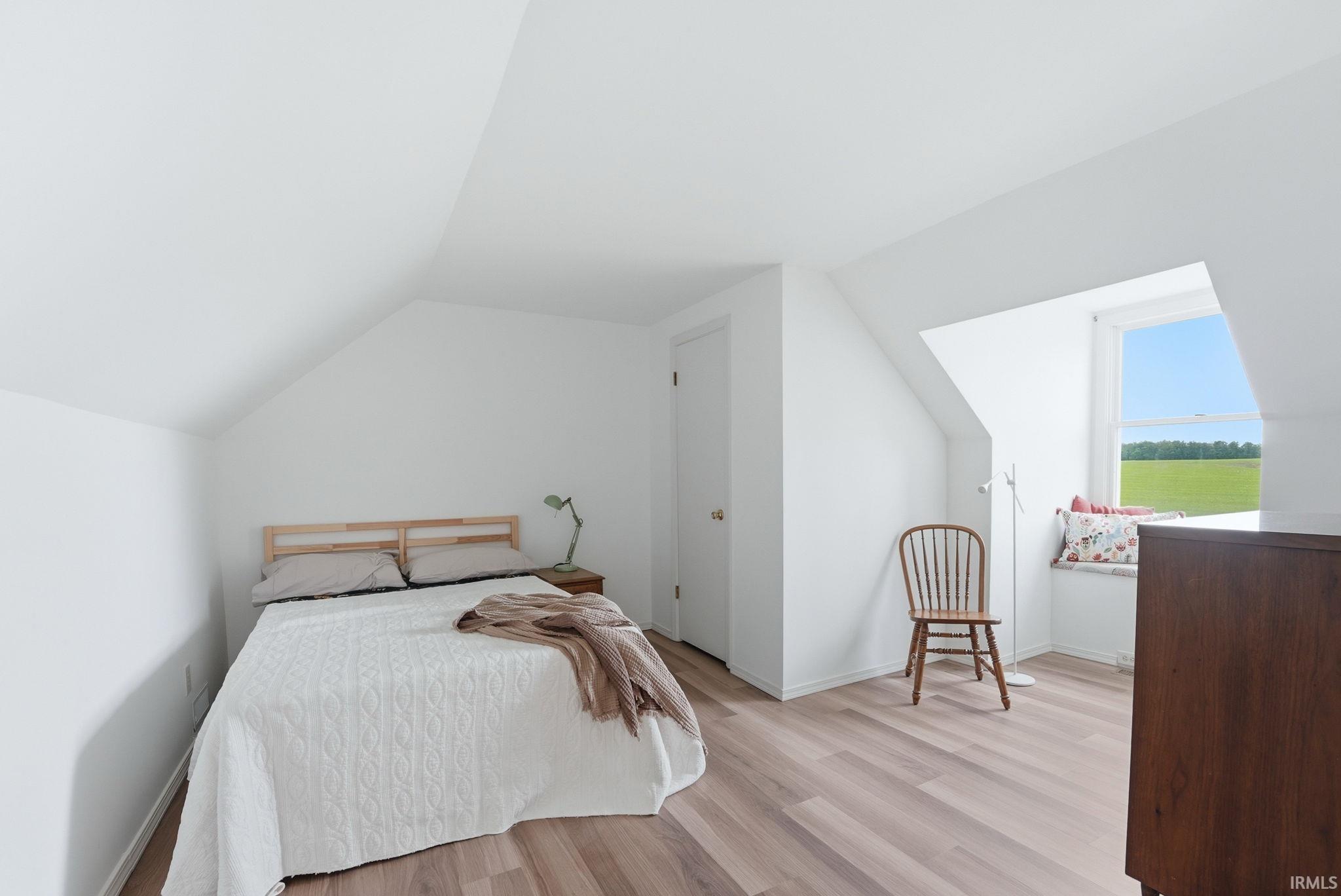 Attic space featuring wood-finish flooring, crisp white walls, and a recessed window with a built-in bench seat