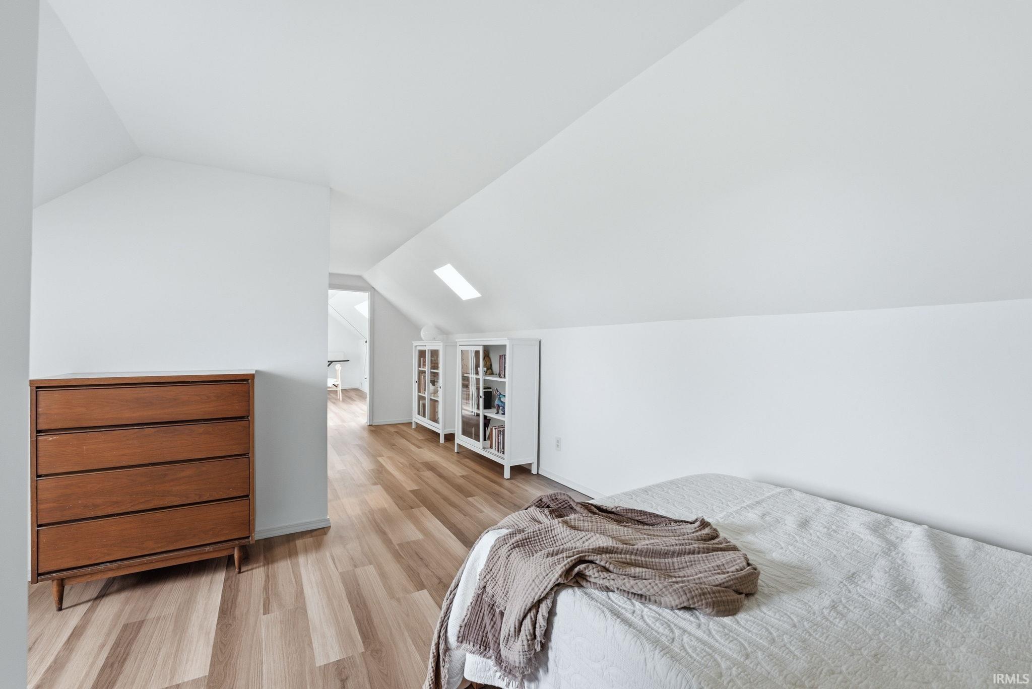 Attic space featuring wood-finish flooring, white sloped ceilings, and a skylight