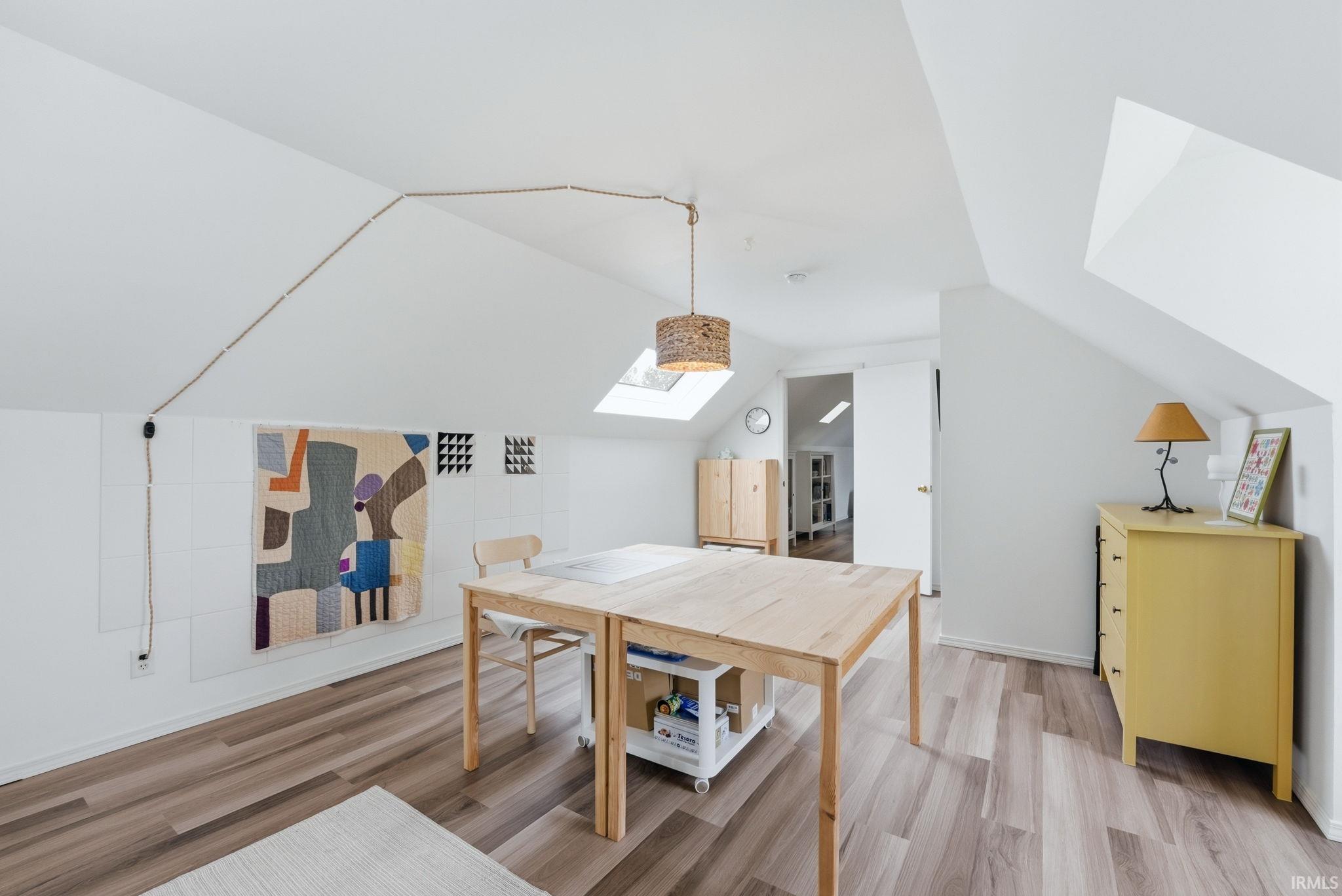 Attic space featuring wood-finish flooring, white vaulted ceilings, and a skylight