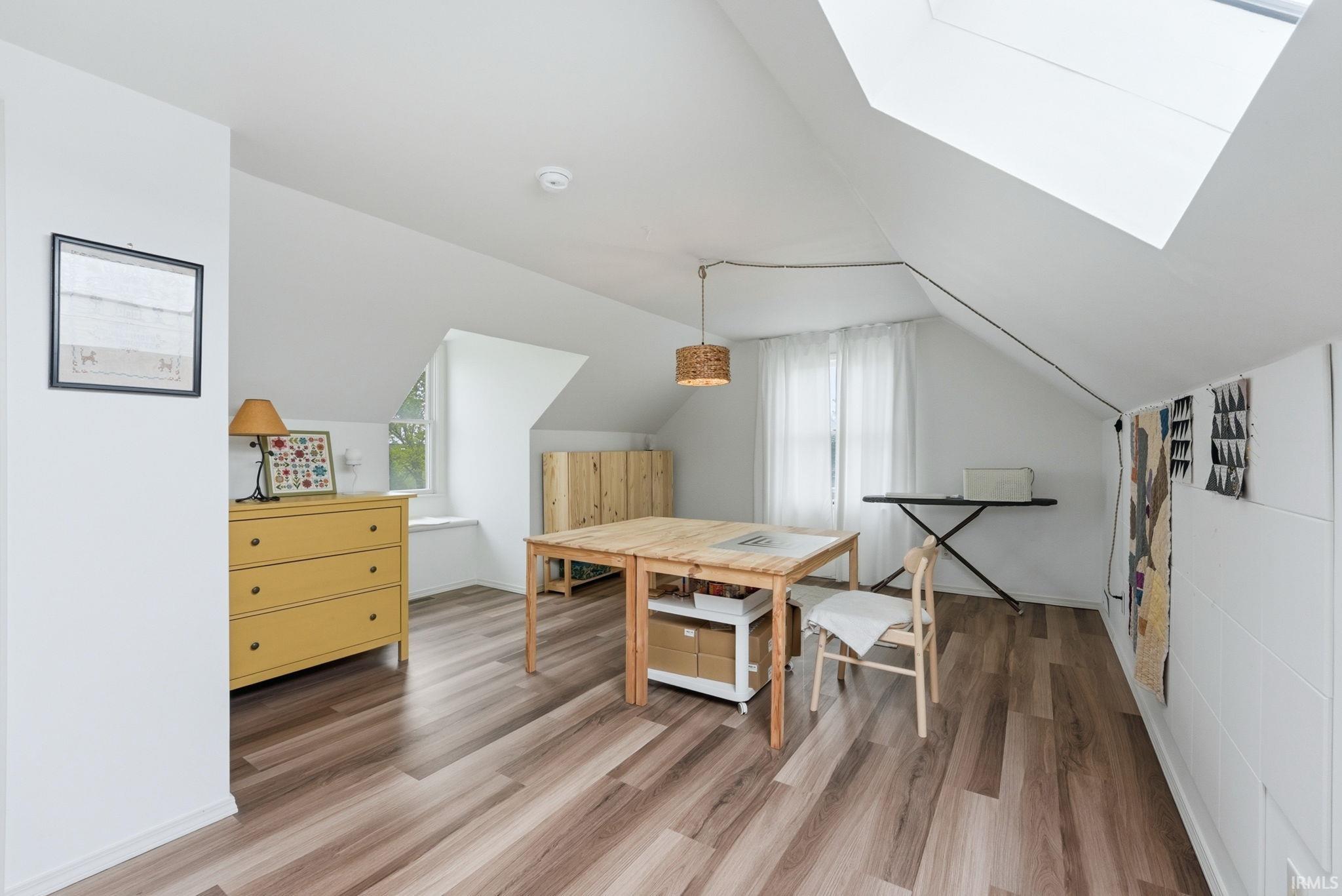 Attic space featuring wood-finish flooring, white walls, and a skylight