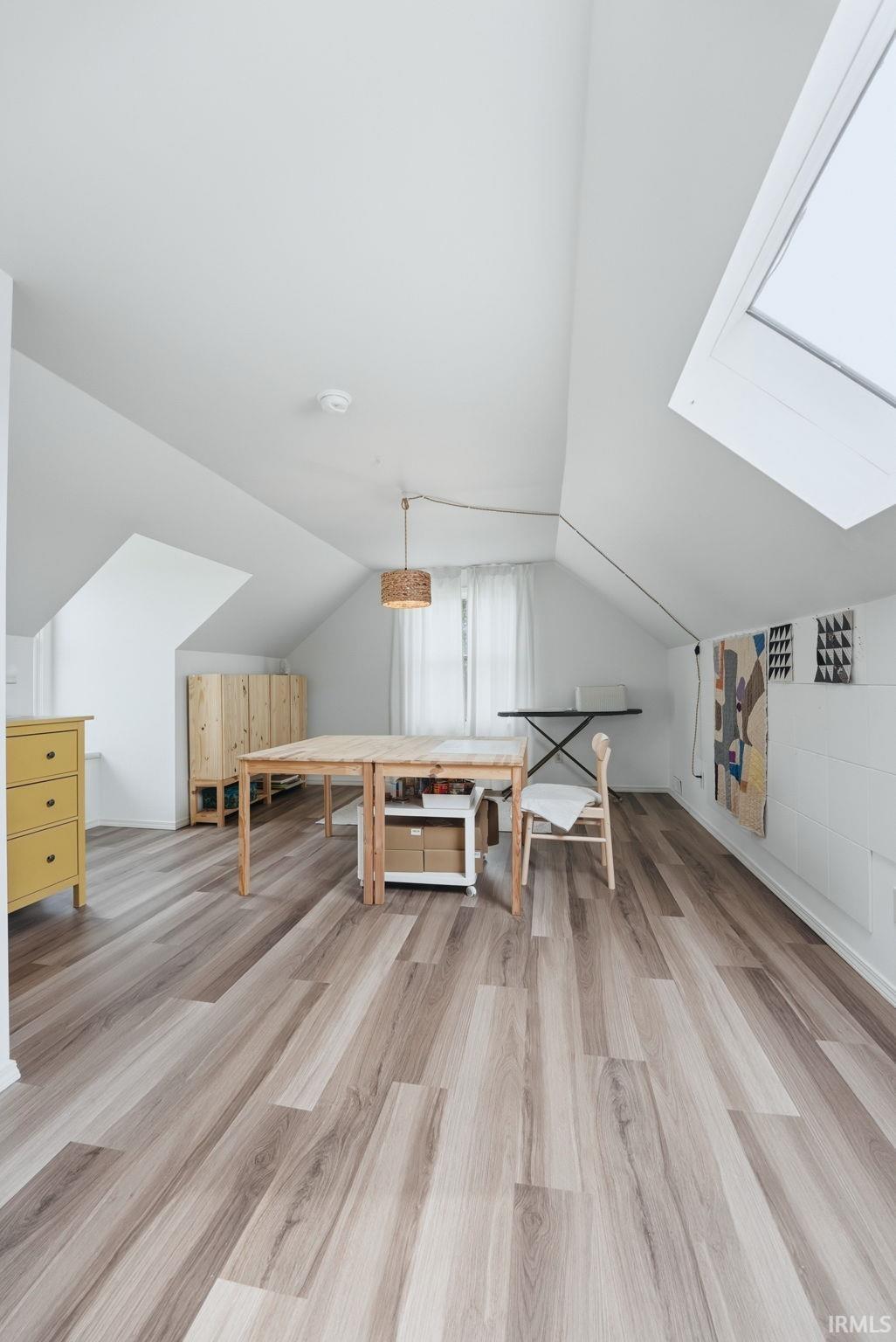 Spacious attic room featuring wood-finish flooring, a skylight, and sloped ceilings