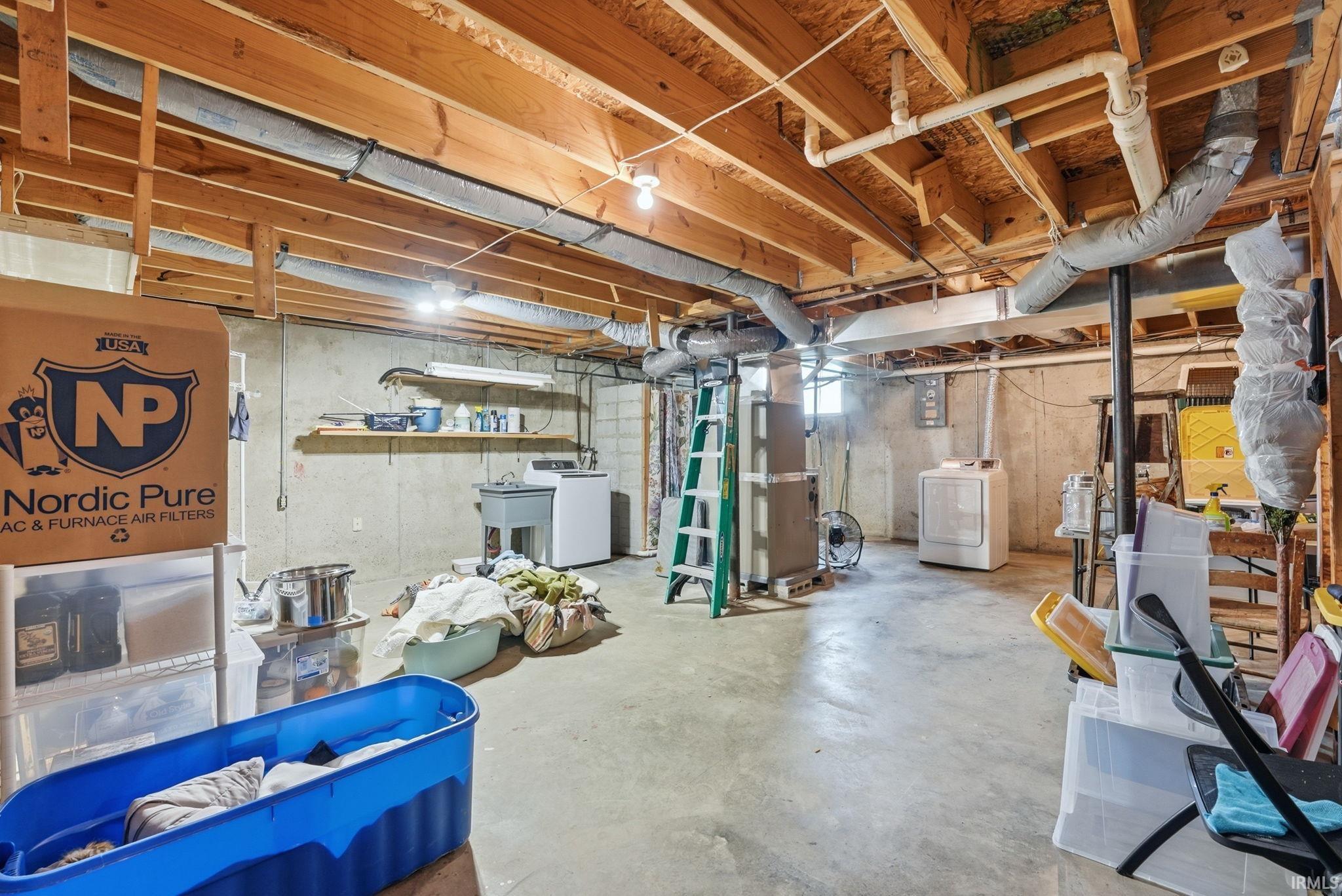 Unfinished basement featuring exposed wood joists, concrete flooring, laundry sink, washer, and dryer