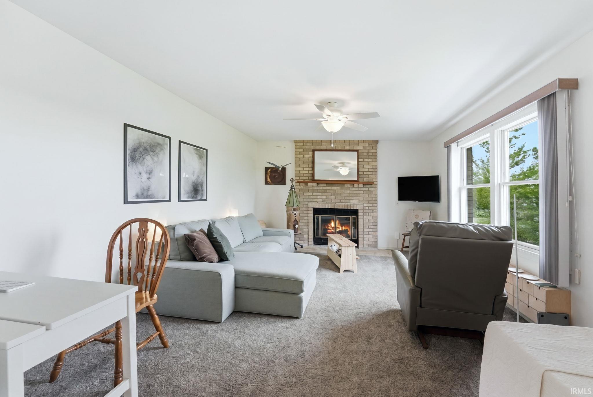 Living area featuring a brick fireplace with a wood mantel, a ceiling fan, and carpet flooring