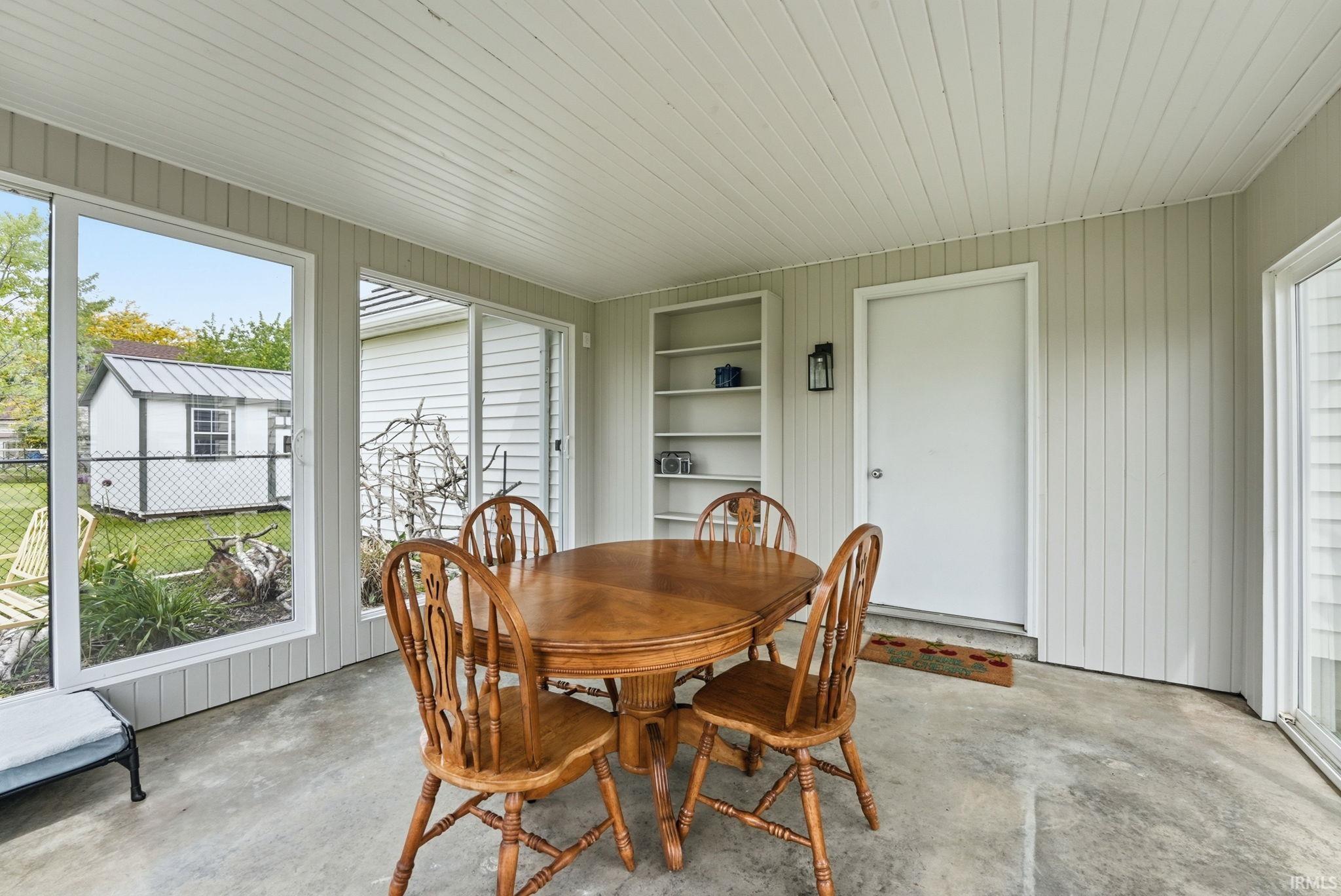 Enclosed patio featuring durable concrete flooring, vertical panel siding, and a beadboard ceiling