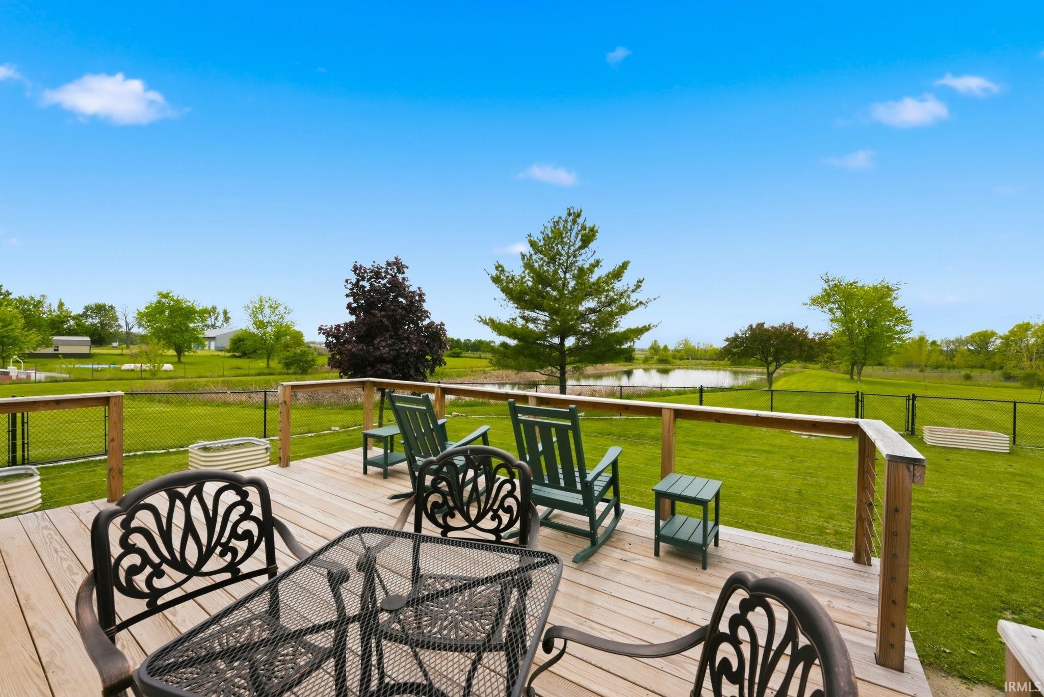 Expansive wood-finish deck with a wooden railing and black chain-link fencing overlooking a large grassy area with mature trees and a pond