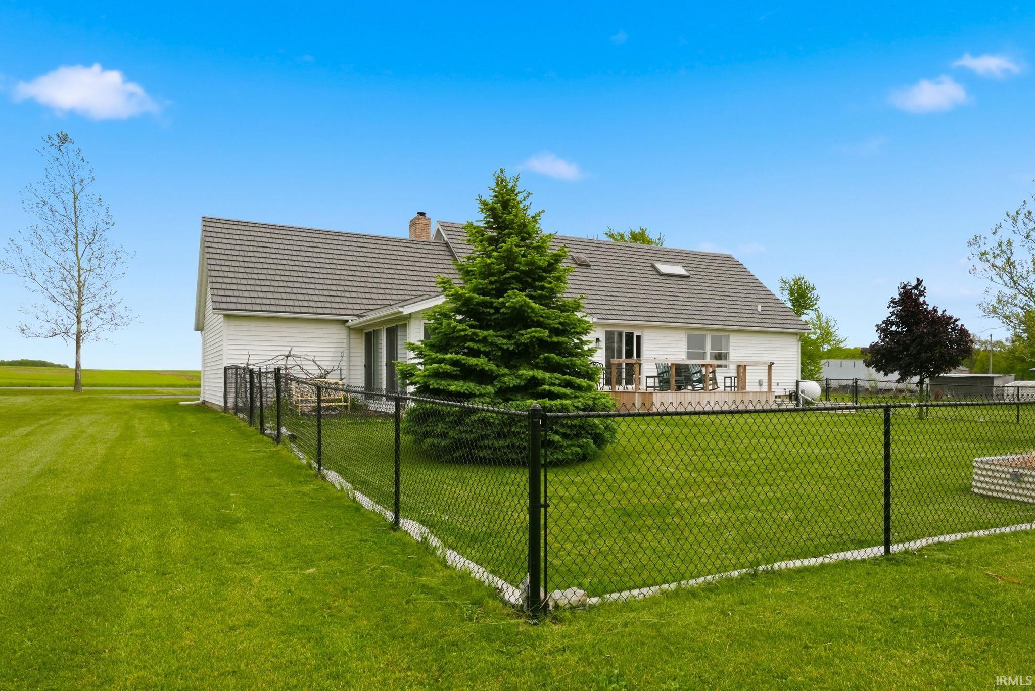 Expansive fenced backyard featuring a wood deck, mature evergreen, and manicured lawn