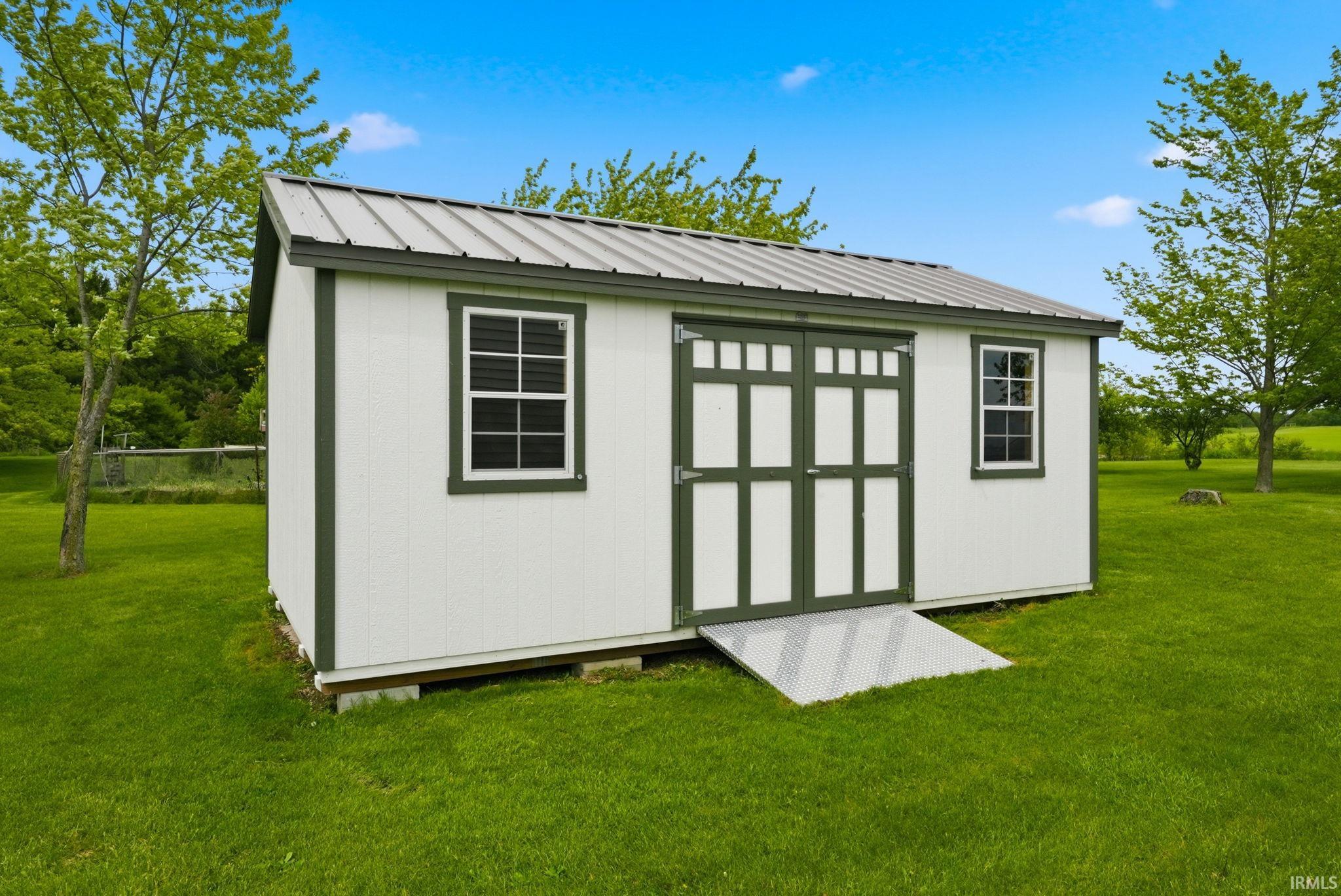 White utility shed with dark green trim, featuring a metal roof and double entry doors