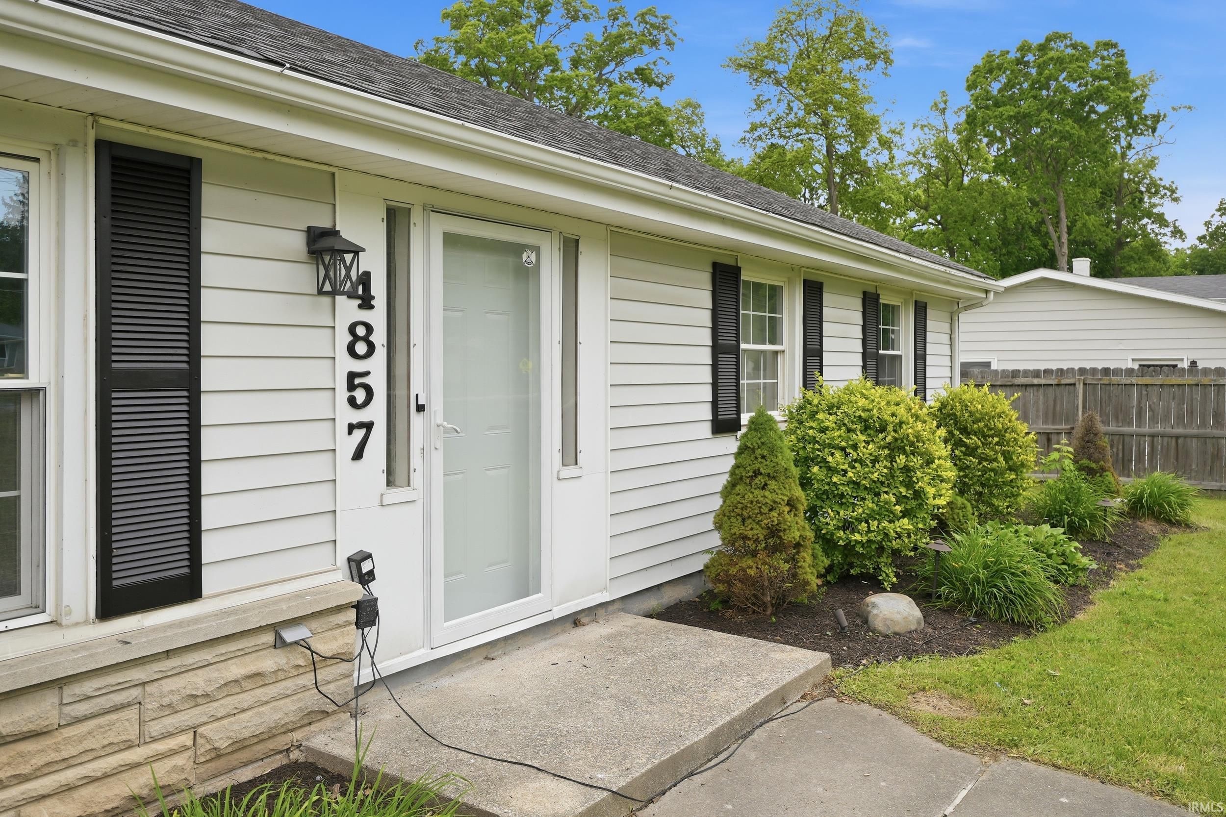White vinyl siding exterior with black louvered shutters and a concrete walkway