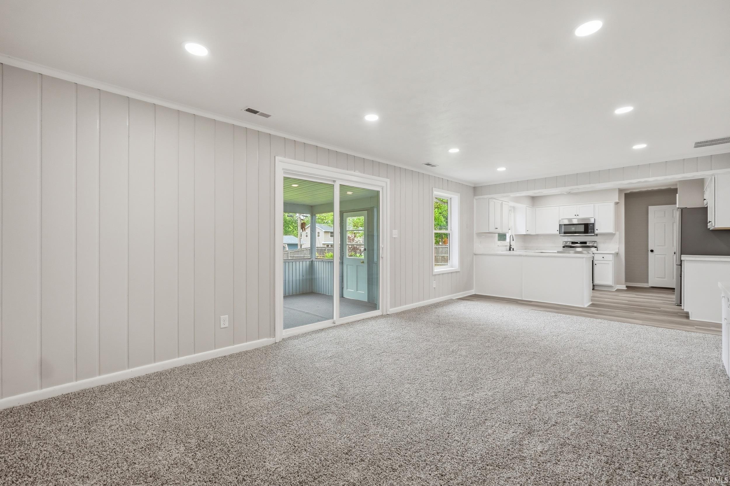 Open concept living area featuring recessed lighting, a sliding glass door, light-toned carpeting, and paneling on the walls