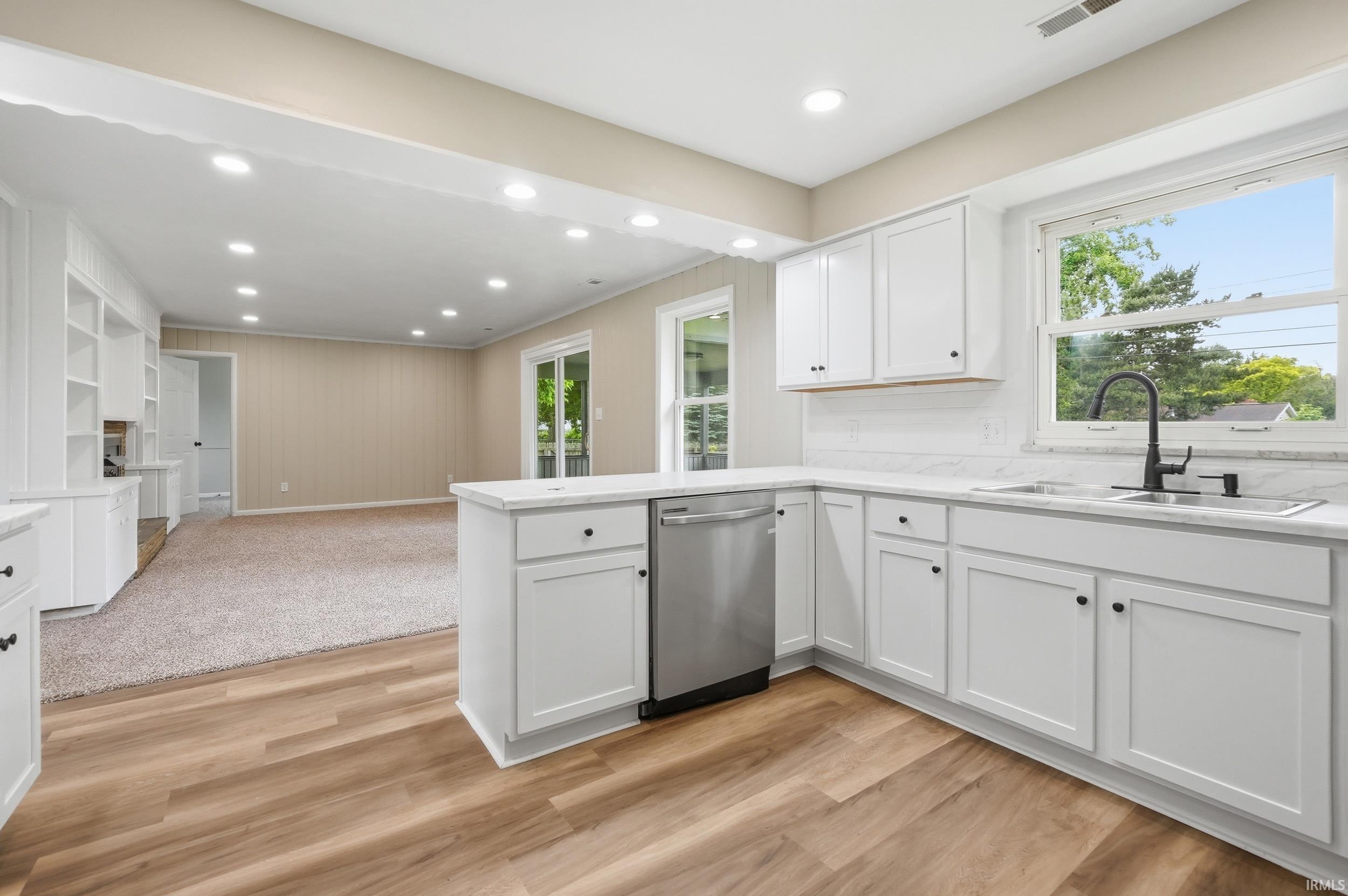 Kitchen featuring white cabinetry, light countertops, stainless steel dishwasher, and wood-finish flooring