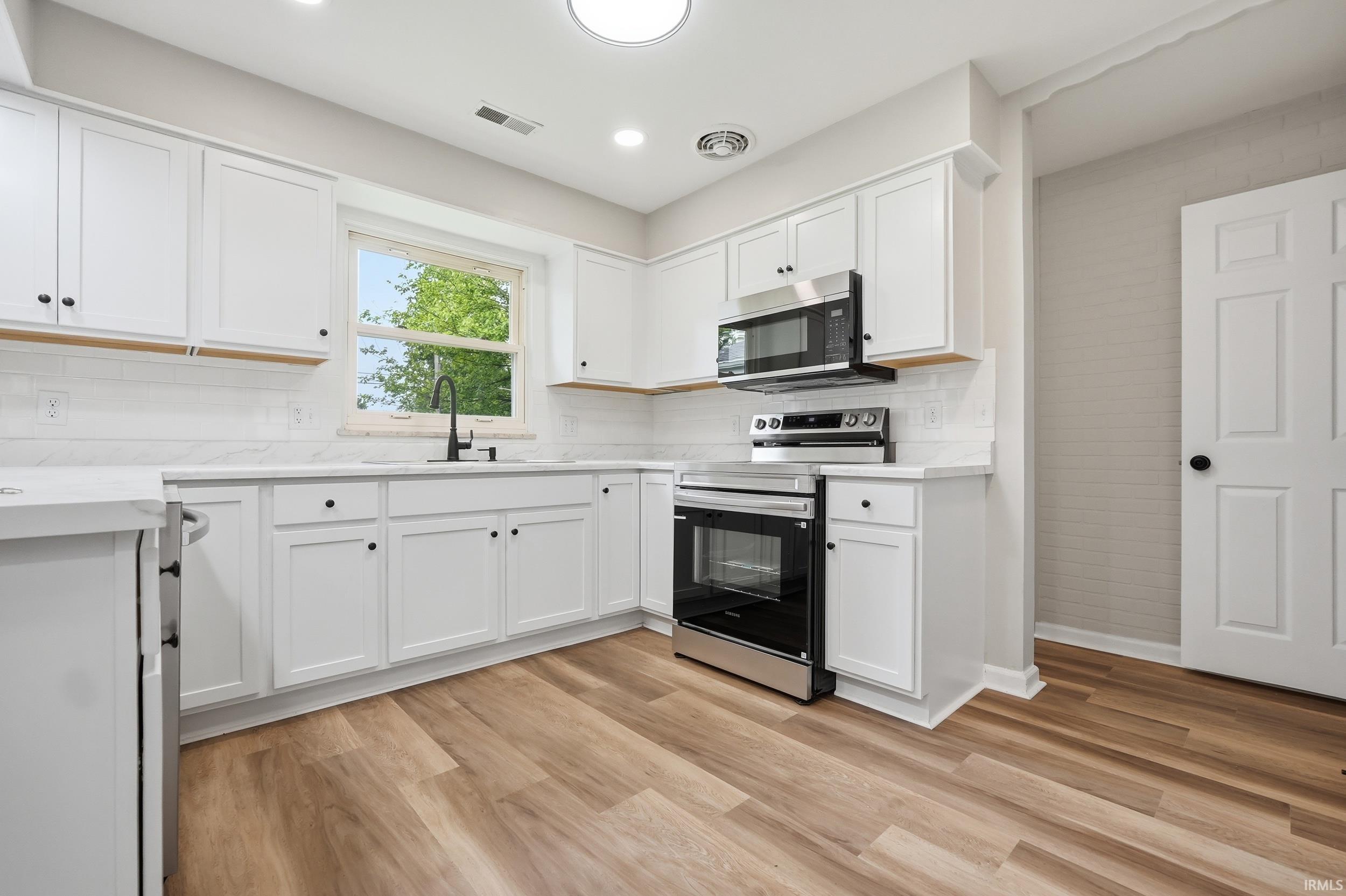 Kitchen featuring white shaker cabinetry, stainless steel appliances, light-toned countertops, a subway tile backsplash, and wood-finish flooring