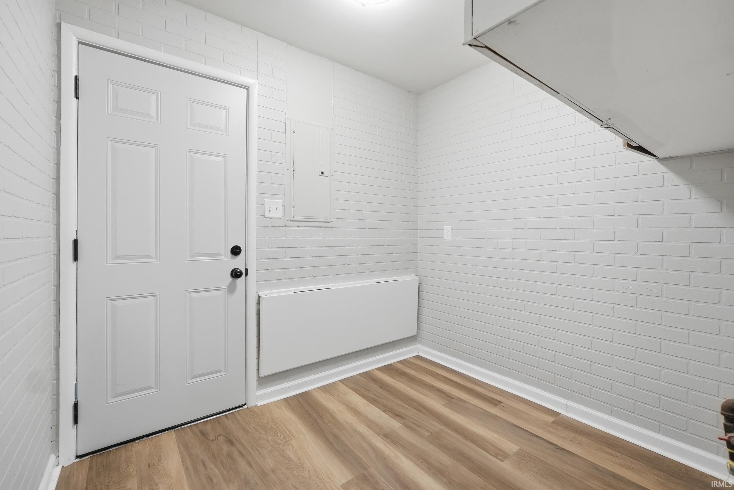White paneled door with black hardware, wood-finish flooring, white brick-patterned walls, and crisp white baseboards