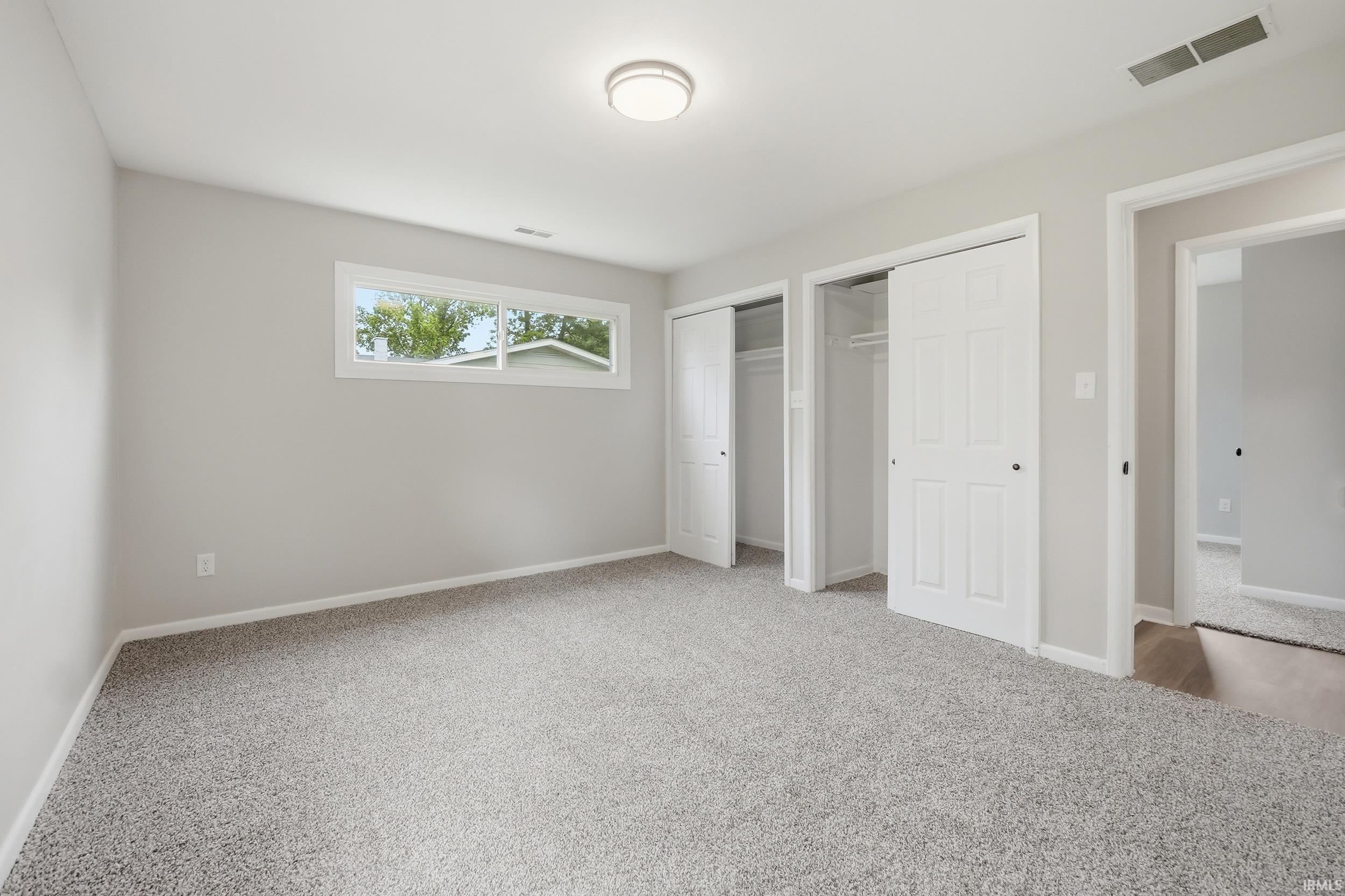 Carpeted room with a horizontal window and two white sliding closet doors