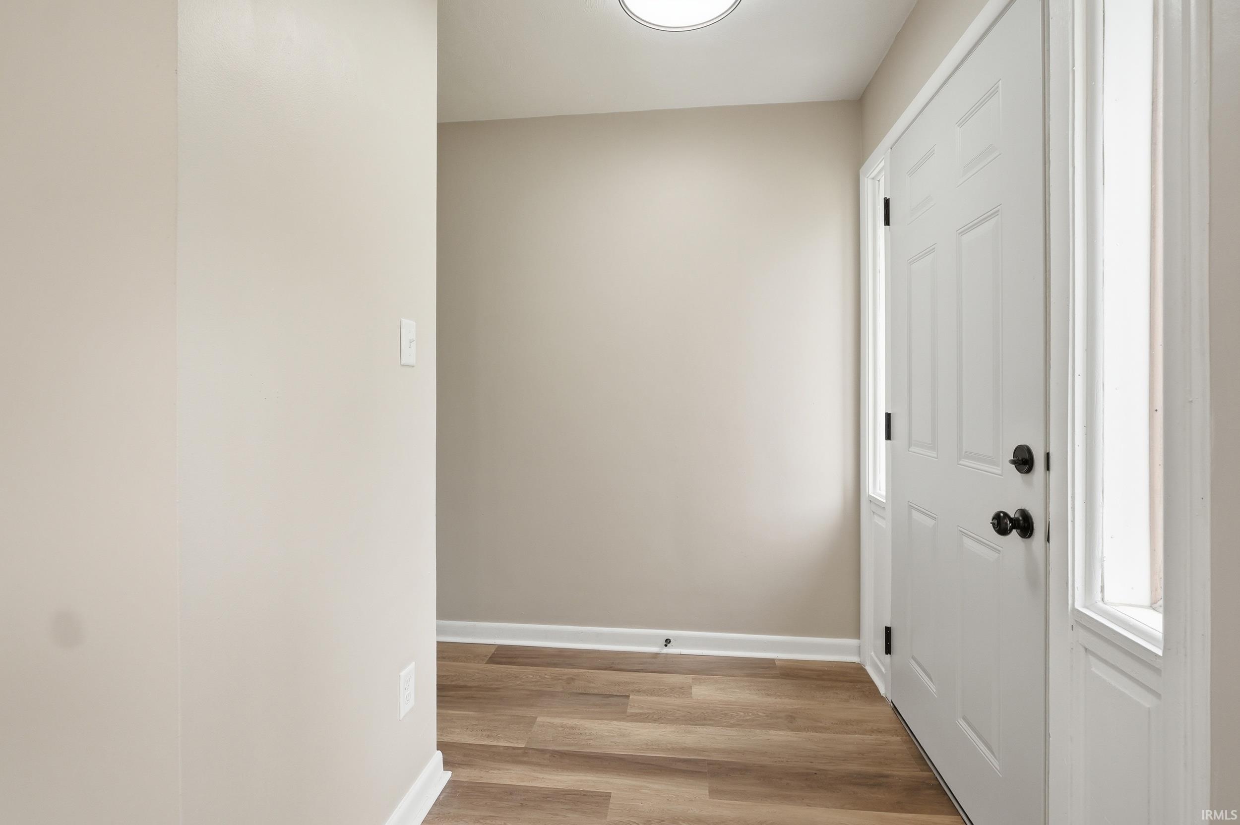Entryway featuring a paneled door with matte black hardware, sidelight windows, wood-finish flooring, and neutral wall paint