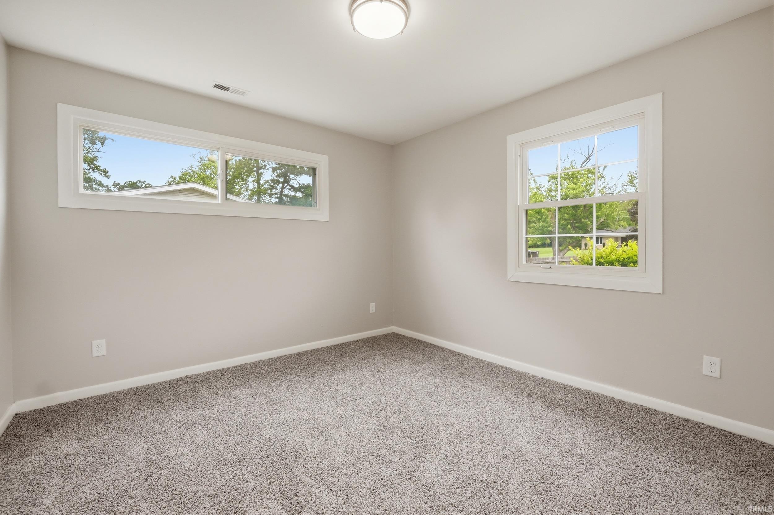Neutral-toned room featuring a flush-mount ceiling light, light gray wall paint, white baseboards, and gray textured carpeting