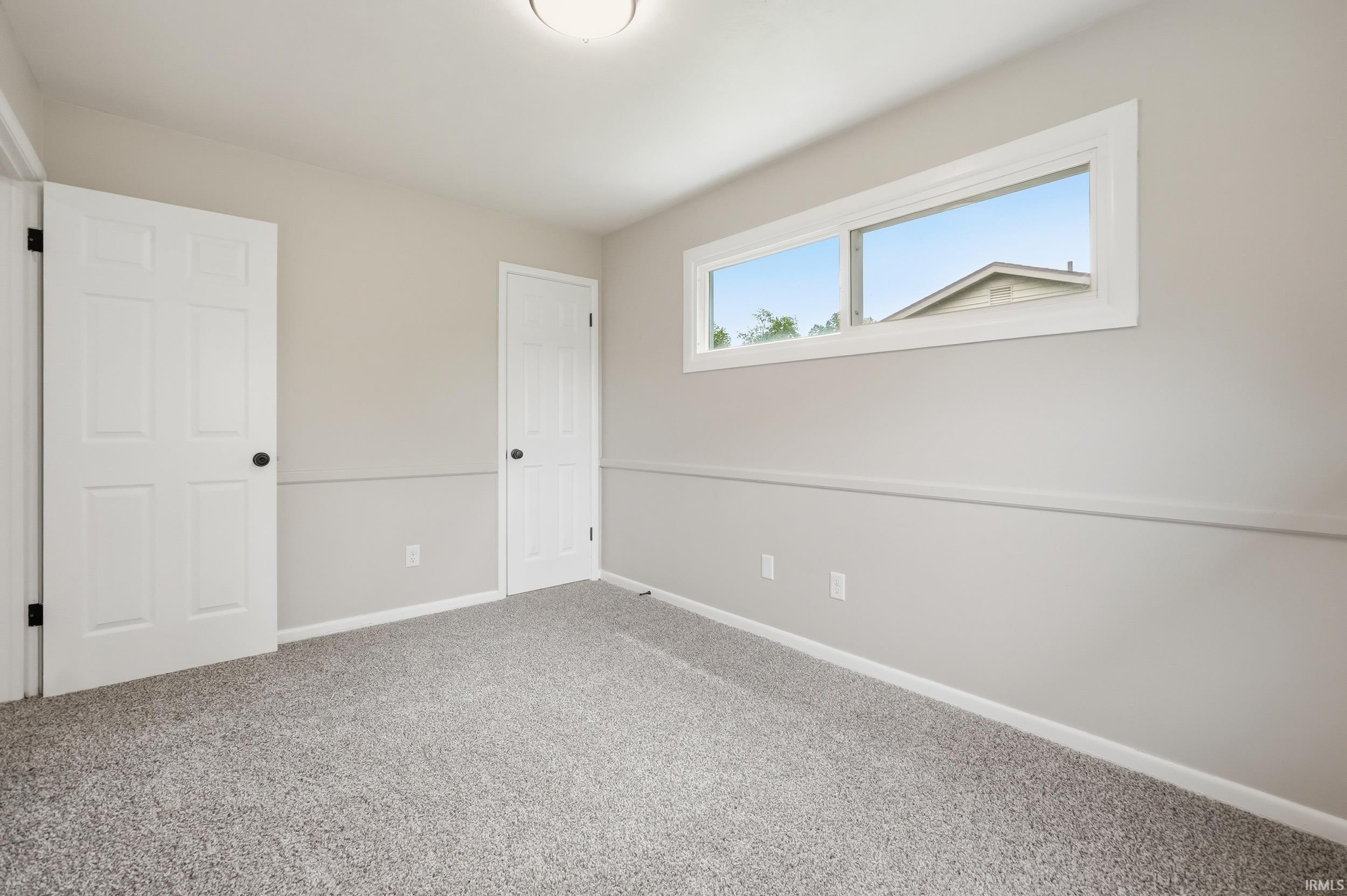 Neutral-toned room featuring a wide window, plush gray carpet, white trim throughout, and two white panel doors with black hardware