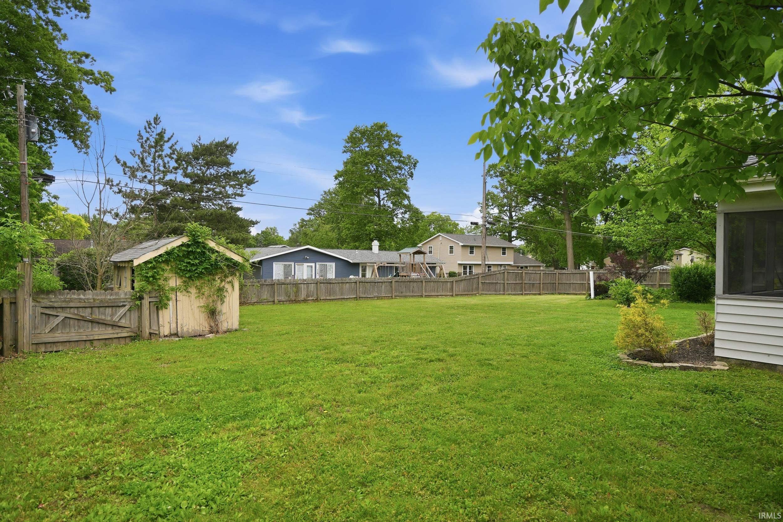 Expansive green lawn featuring a wooden storage shed, perimeter wood fencing, and mature trees