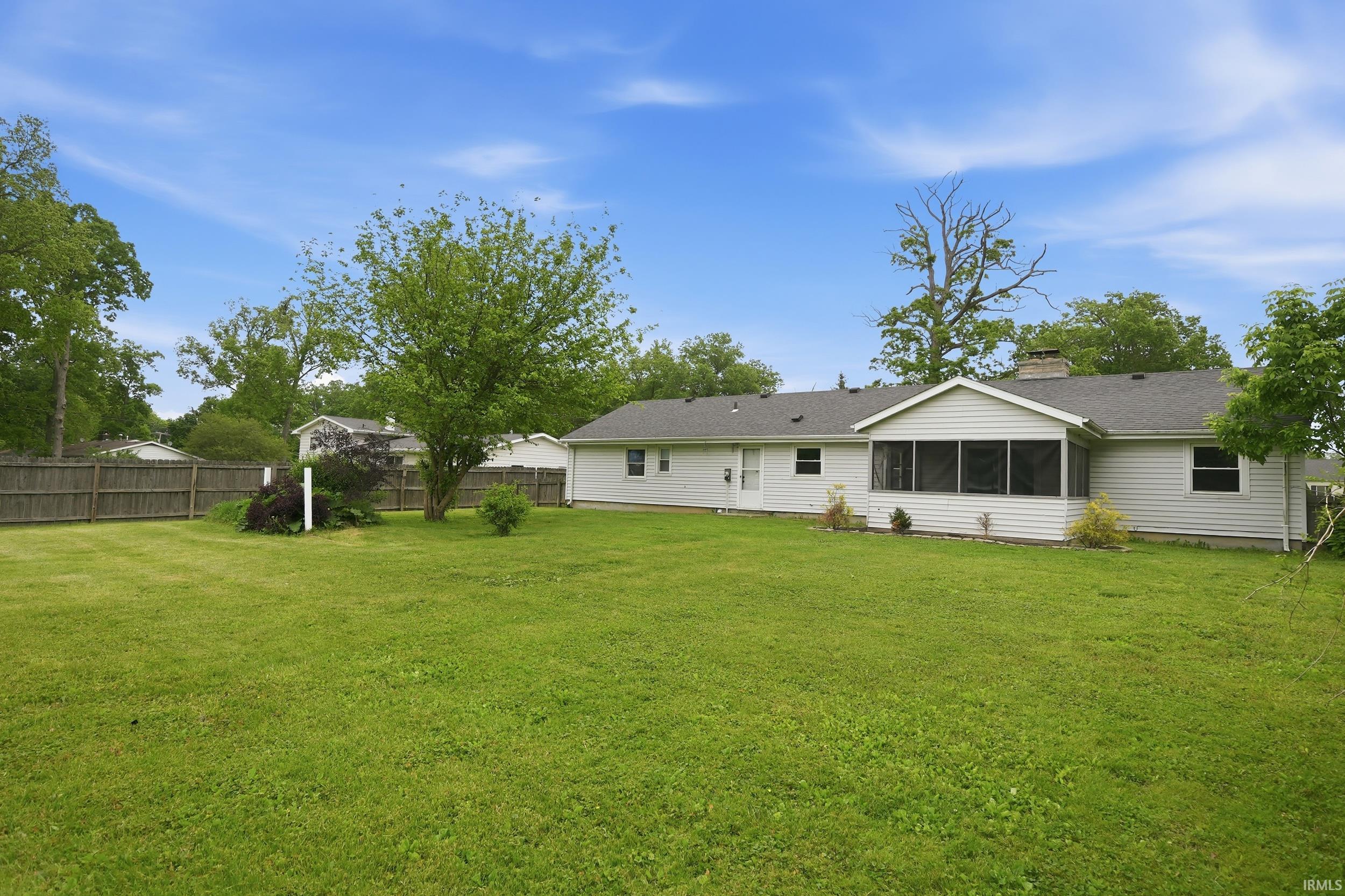 Expansive backyard featuring a large green lawn, mature trees, and a full privacy fence