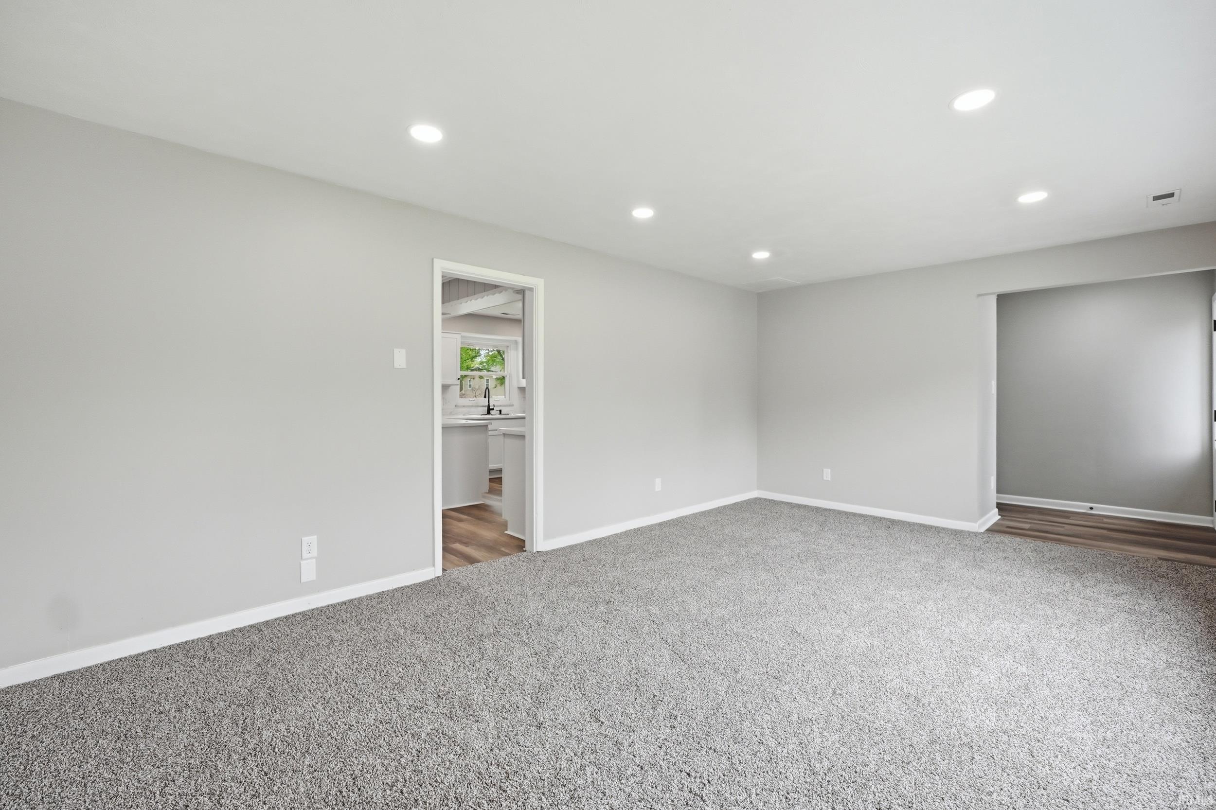 Spacious room featuring light gray walls, recessed lighting, and gray carpeting