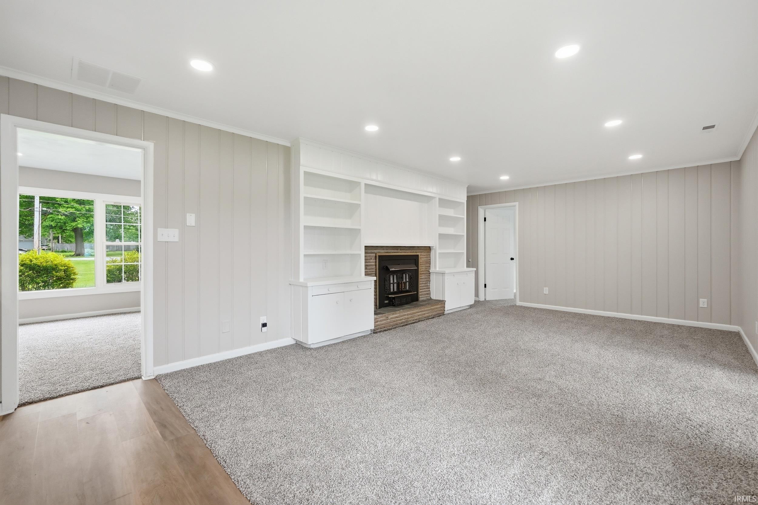 Spacious room featuring light gray vertical paneling, recessed lighting, built-in shelving, a brick fireplace, and gray carpet flooring