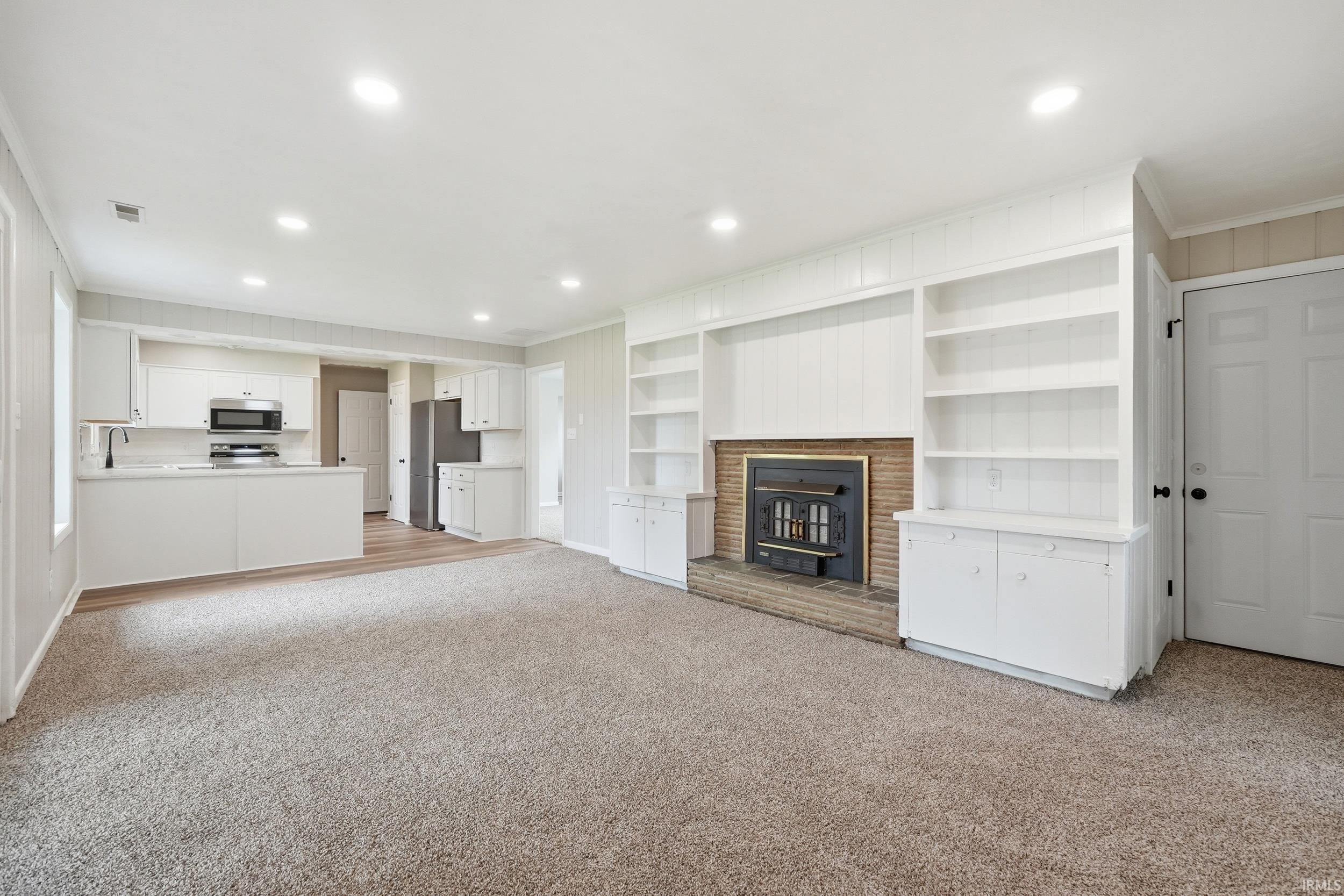 Spacious living area featuring a wood-burning fireplace with a brick surround, built-in shelving, and recessed lighting