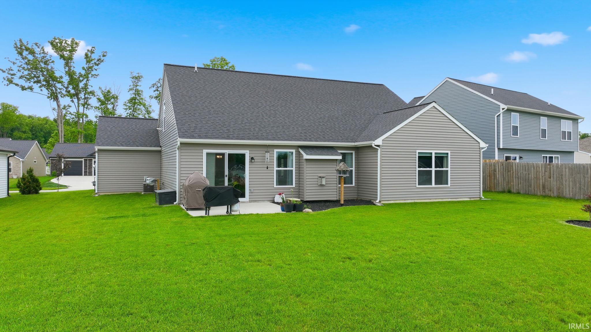 Expansive green lawn surrounds the rear of the property, featuring gray siding, a dark shingle roof, and a concrete patio