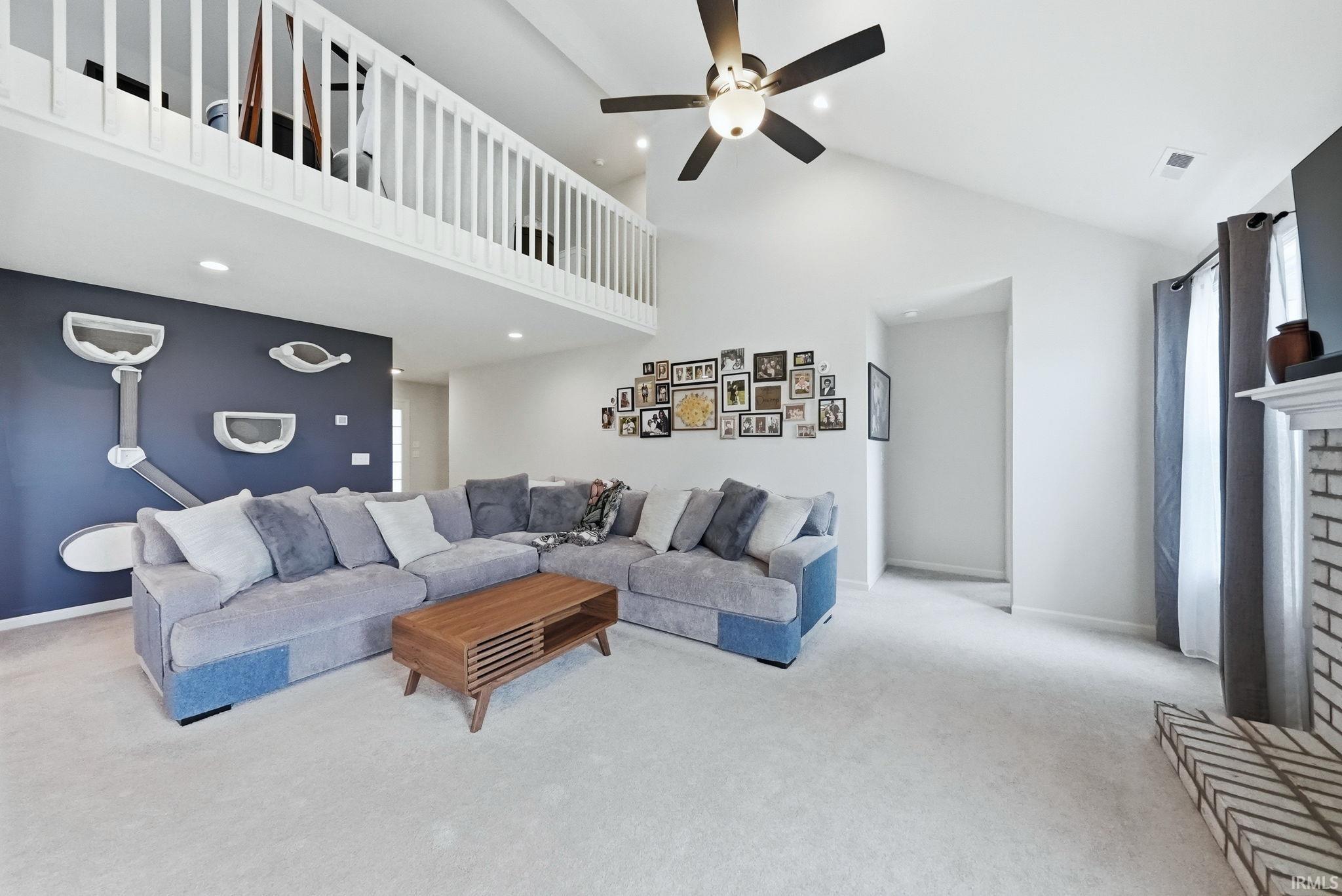 Vaulted ceiling with a ceiling fan, white spindle railing overlooking the room, recessed lighting, and a white brick fireplace with a mantel