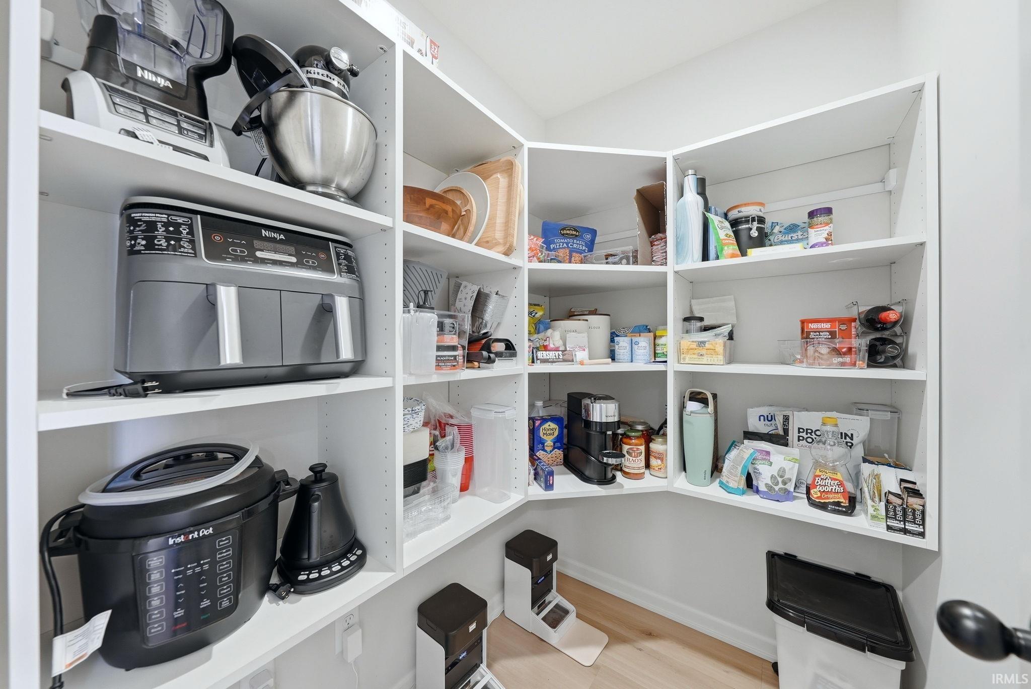 Walk-in pantry featuring white shelving, light wood-finish flooring, and a white baseboard