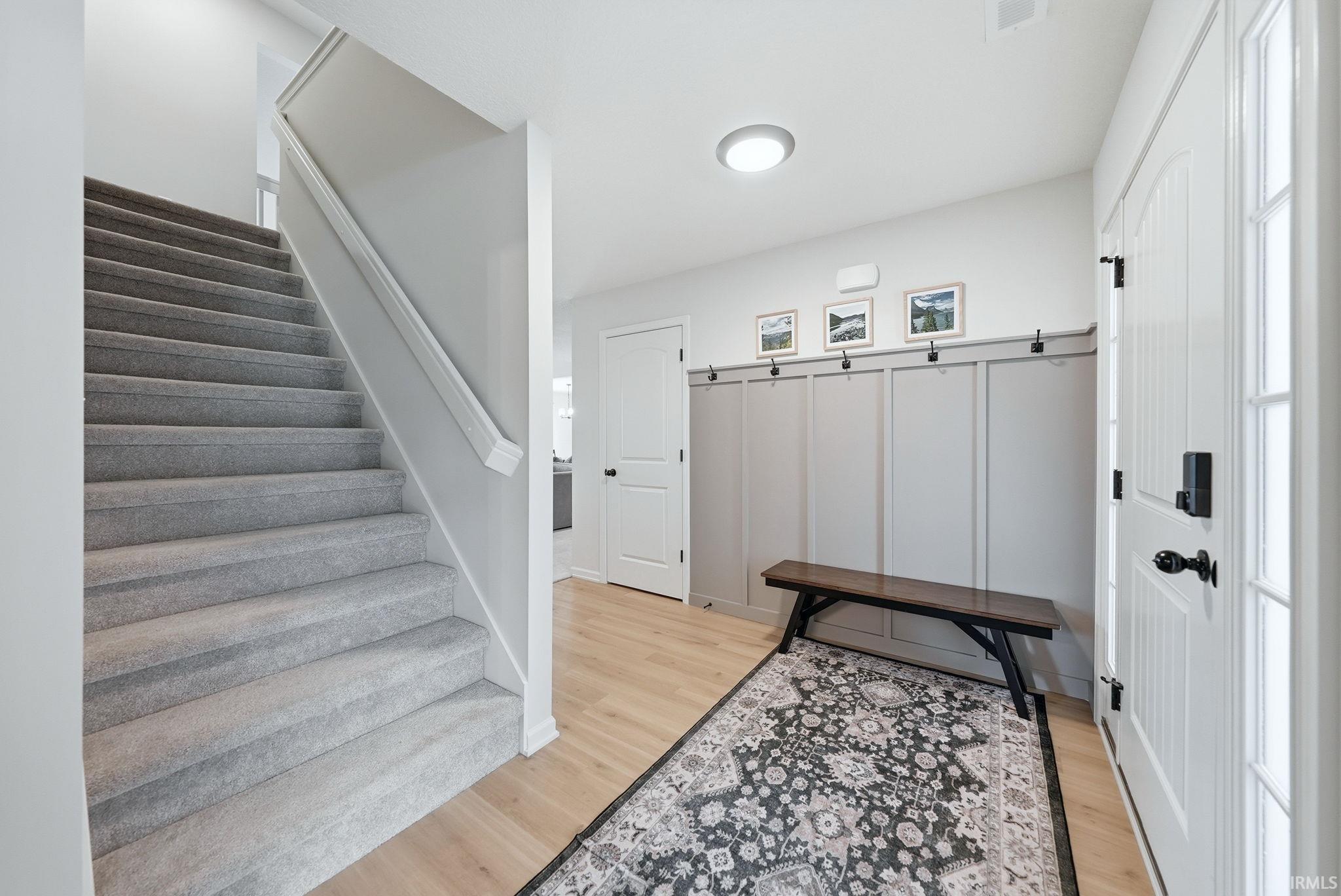 Foyer with light wood-finish flooring, a built-in board and batten wall with coat hooks, and a white paneled entry door with sidelight