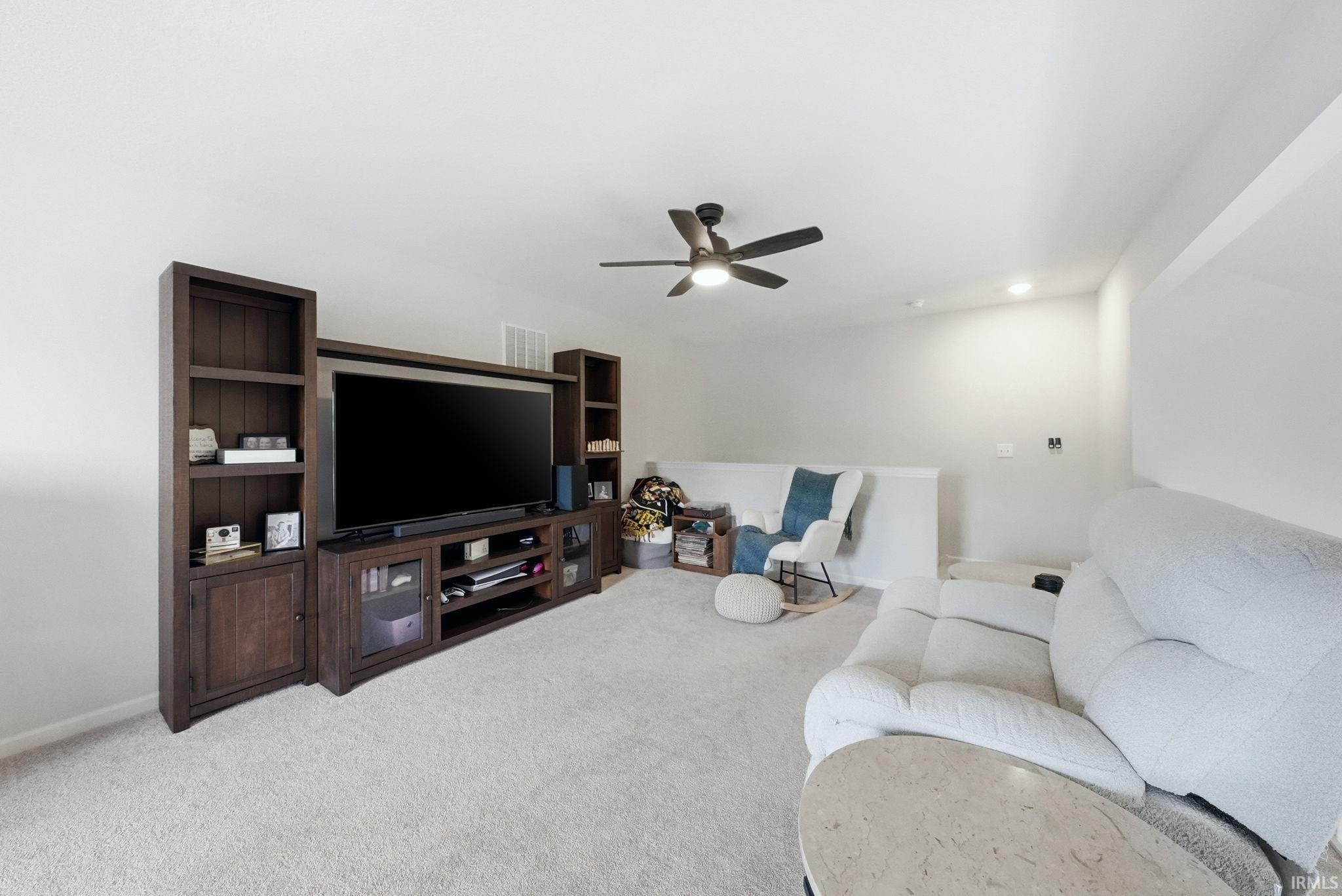 Expansive entertainment area featuring a ceiling fan with integrated lighting, recessed lighting, neutral carpeting, and a built-in media console with shelving