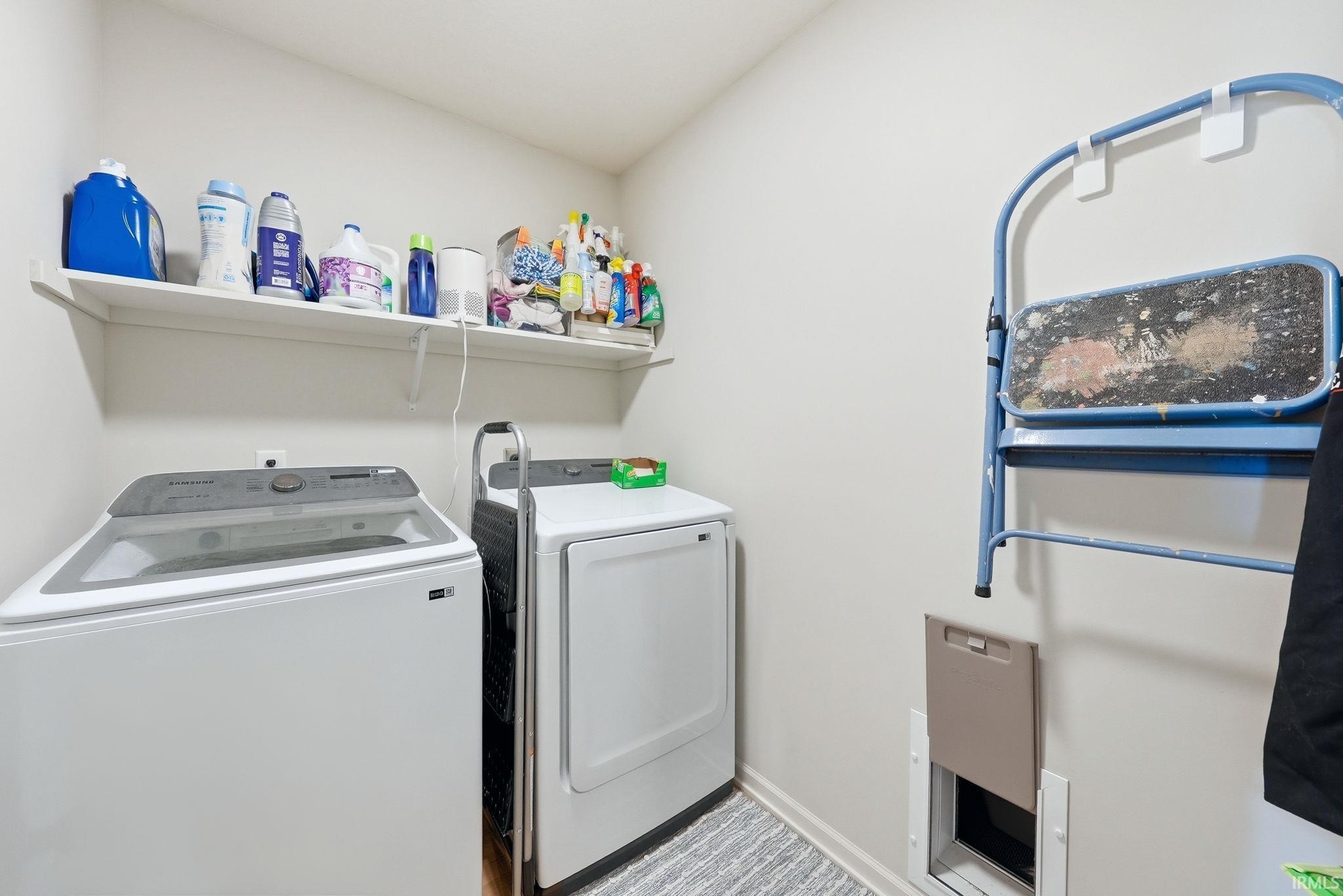Dedicated laundry area featuring a white wall shelf, light-toned walls, and a built-in pet door