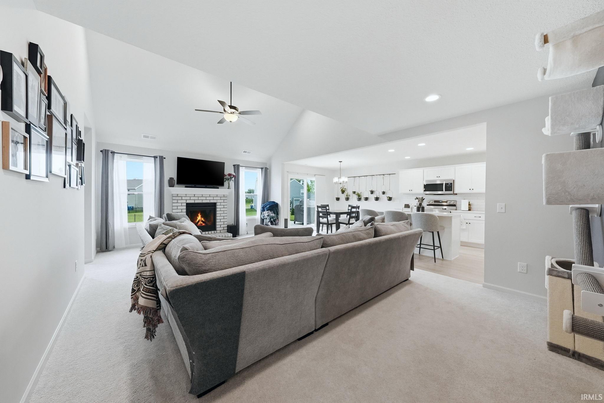 Open-concept living space featuring a vaulted ceiling and a white brick fireplace