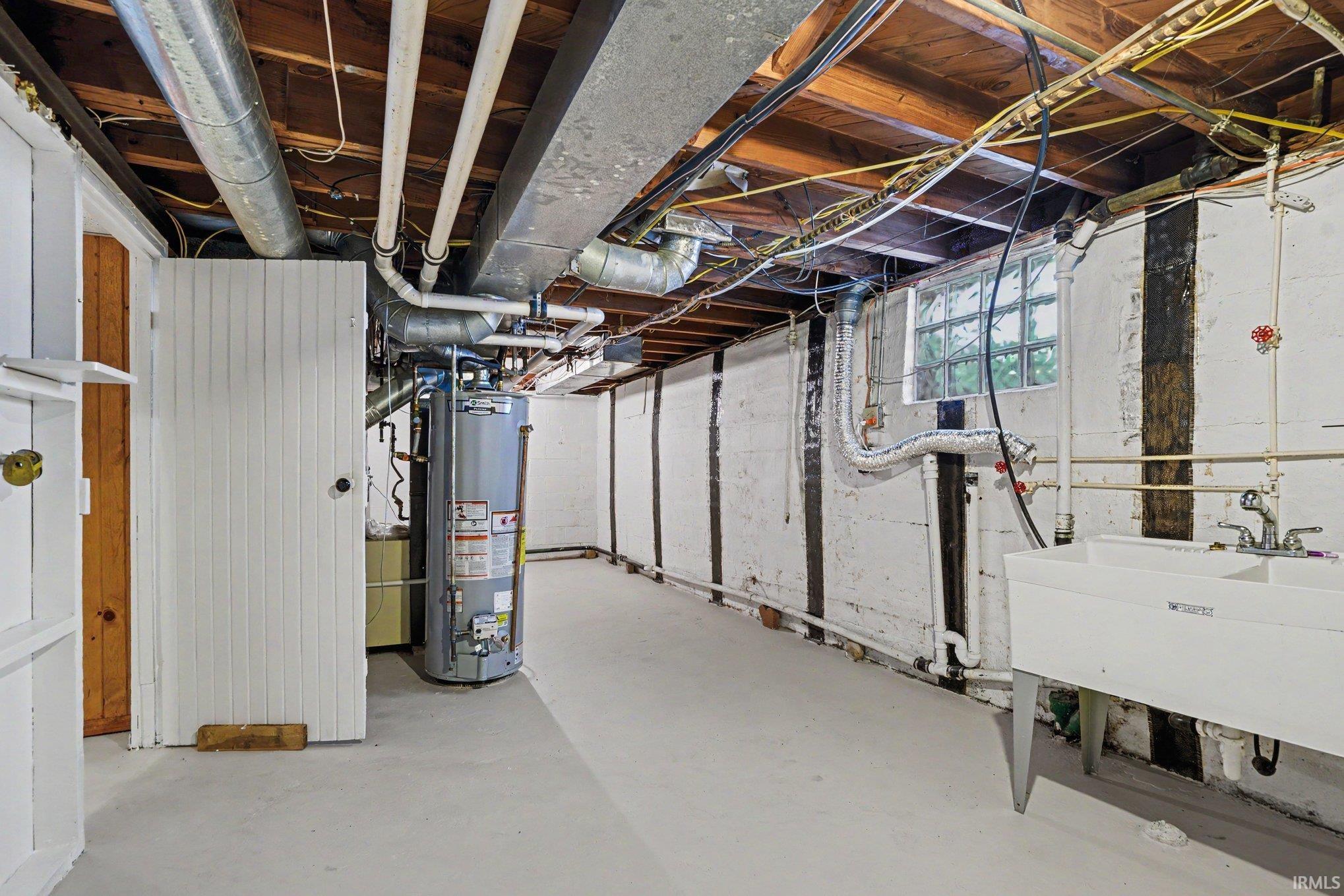 Utility area featuring a water heater, exposed overhead ductwork, and a laundry sink with a double basin
