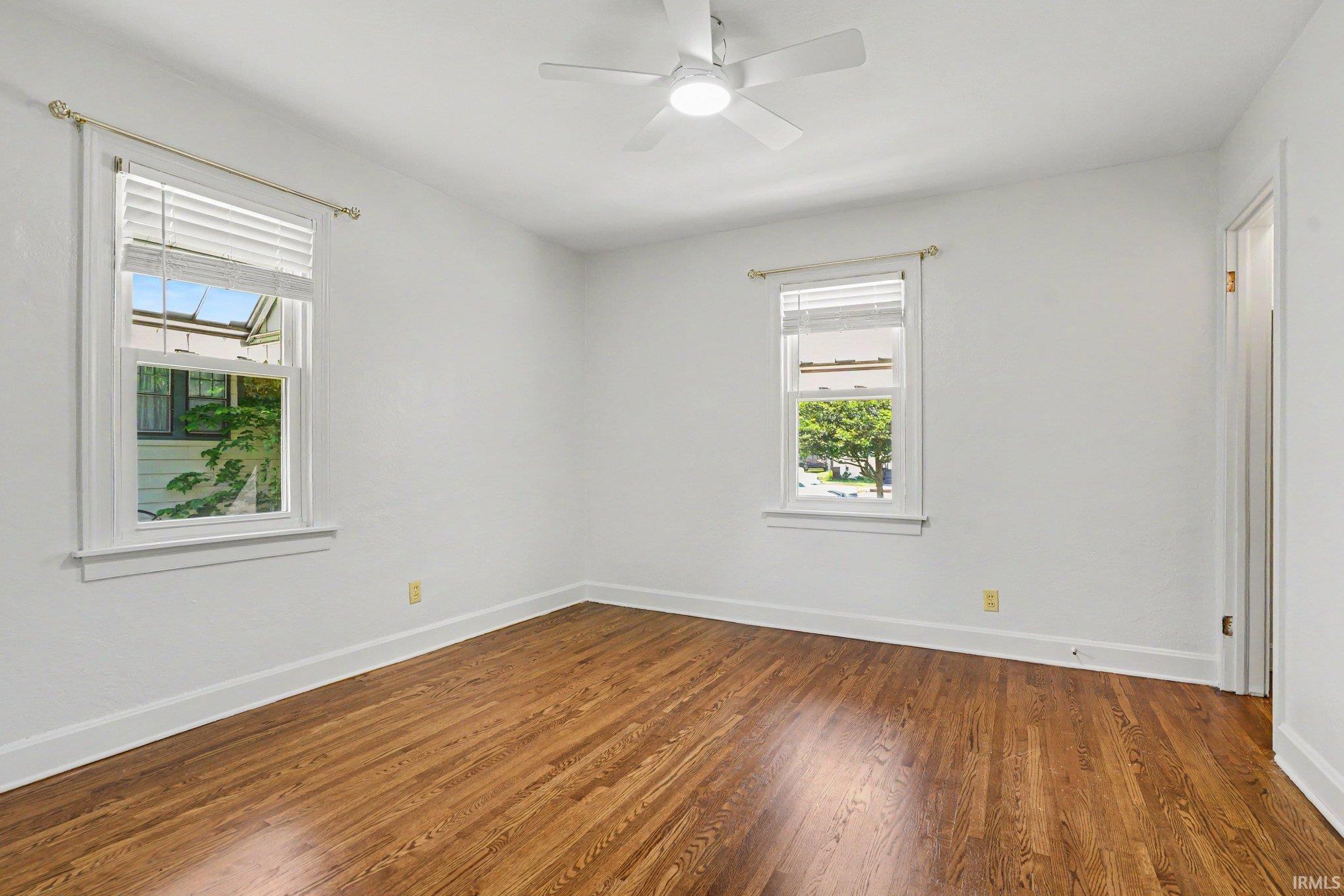 Room featuring wood-finish flooring, two windows with white blinds, and a ceiling fan with integrated lighting