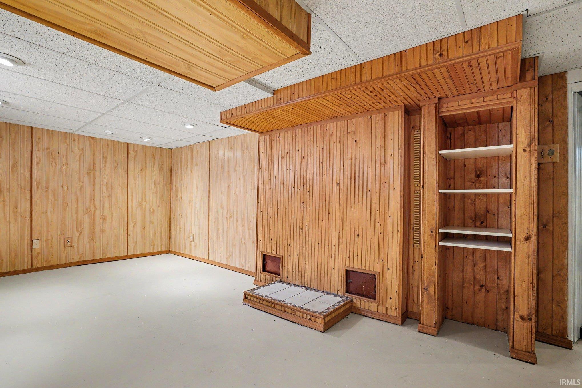 Interior room featuring wood paneling throughout, built-in shelving, dropped ceiling with recessed lighting, and a light-colored flooring