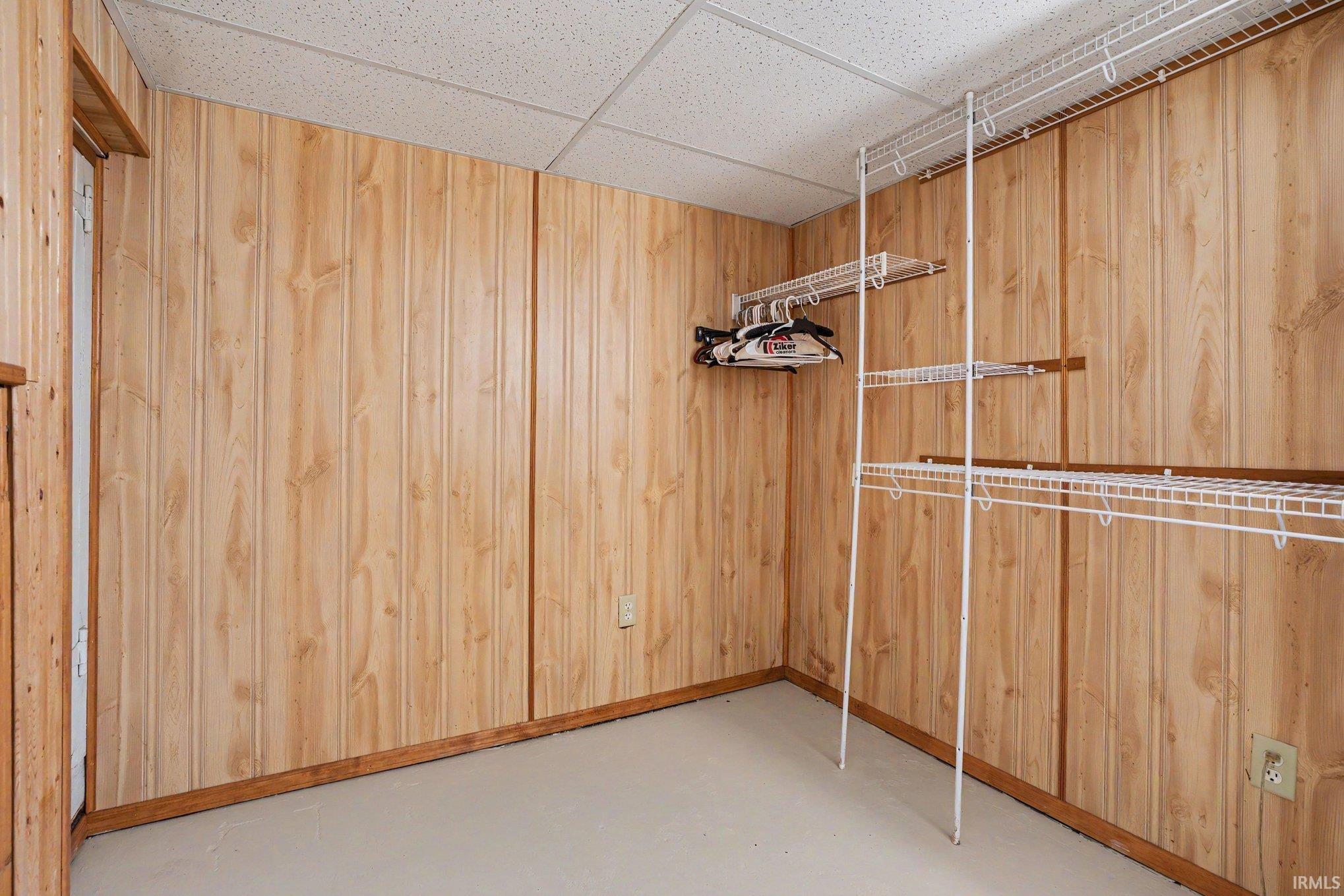 Room featuring light wood paneling, a drop ceiling, and light-colored flooring