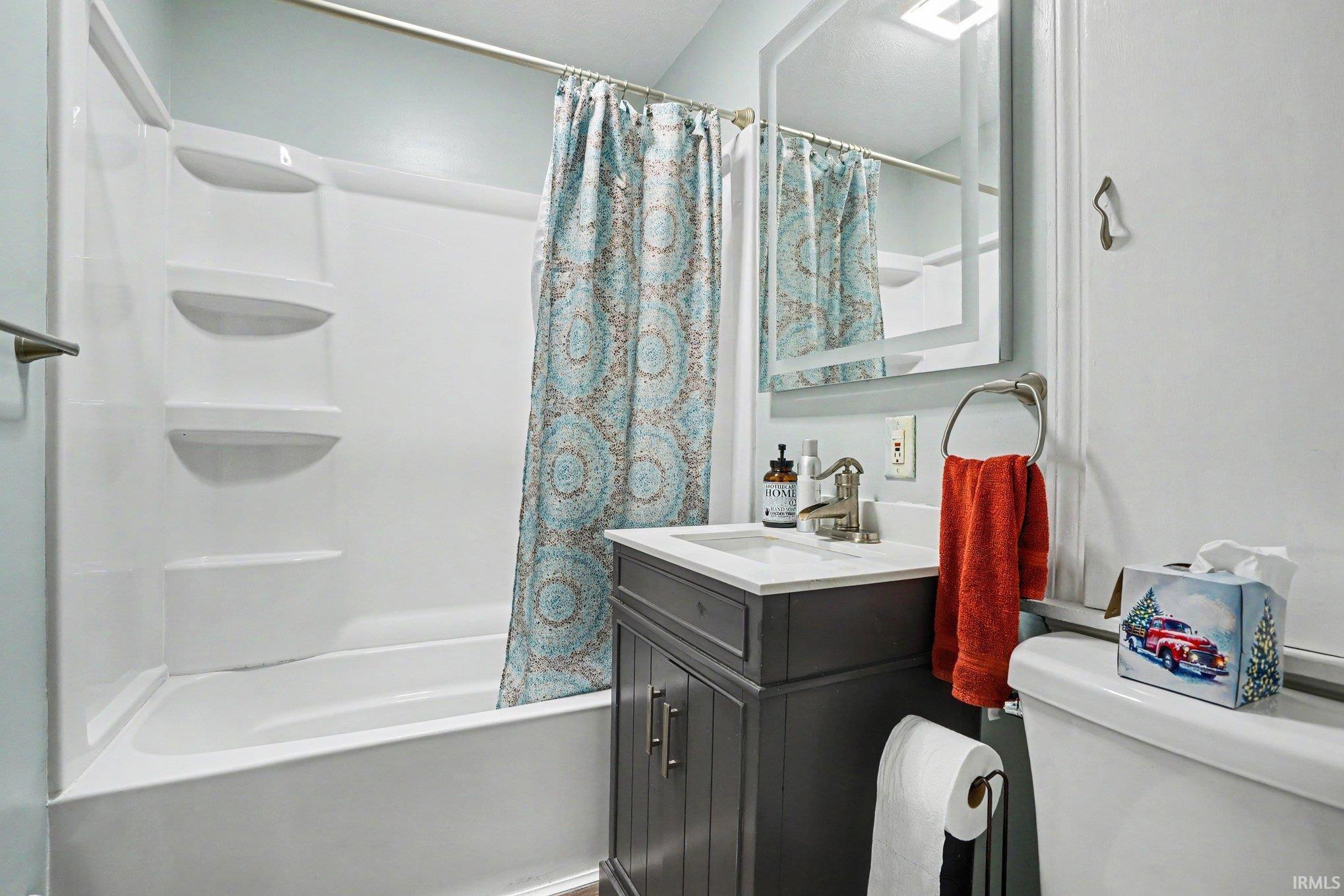 Bathroom featuring a white tub/shower combination, dark wood-finish vanity with an integrated white sink, brushed nickel faucet, and a wall-mounted mirror