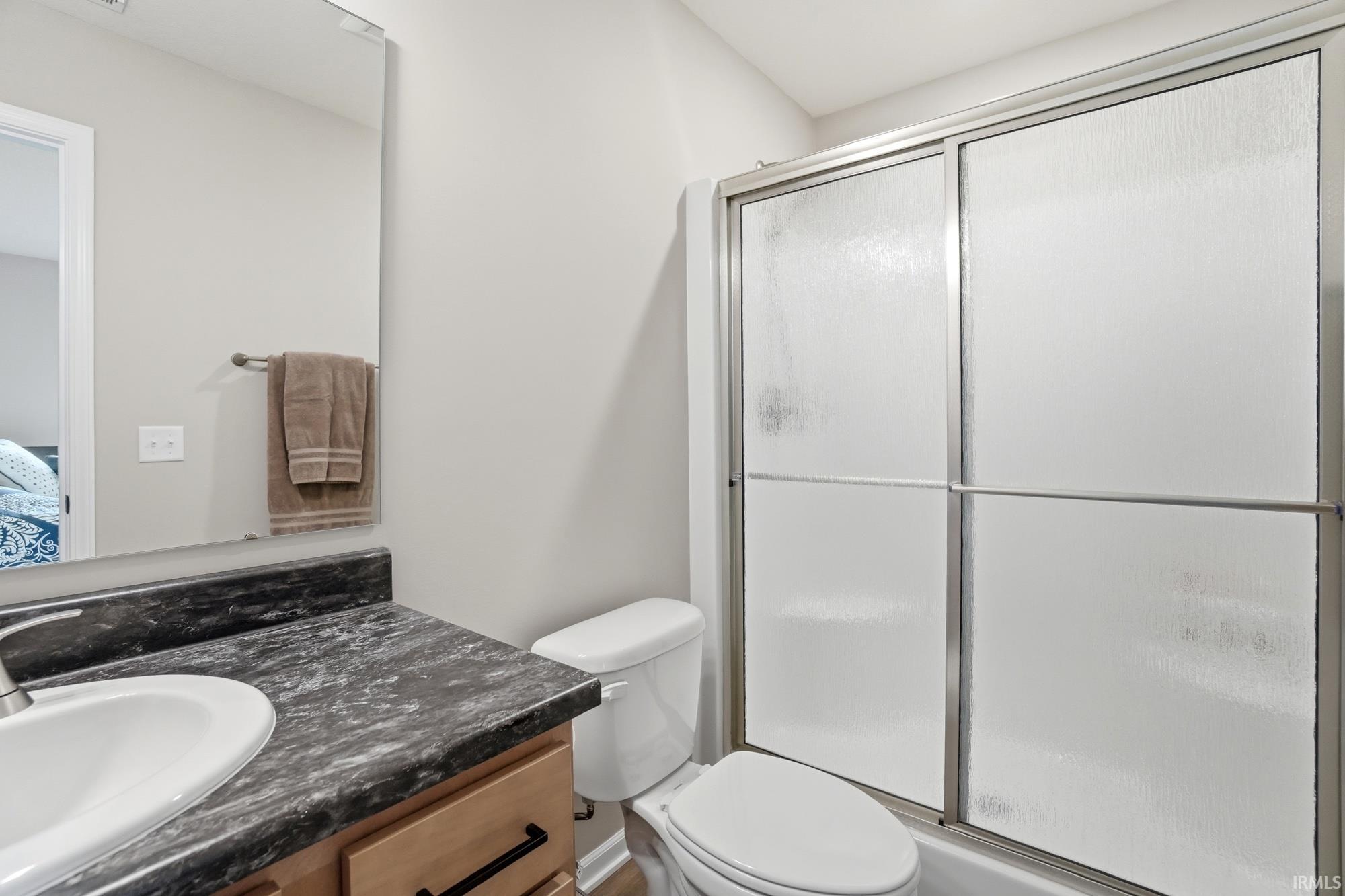 Bathroom featuring a vanity with dark patterned countertop and integrated sink, a commode, and a shower with sliding opaque glass doors