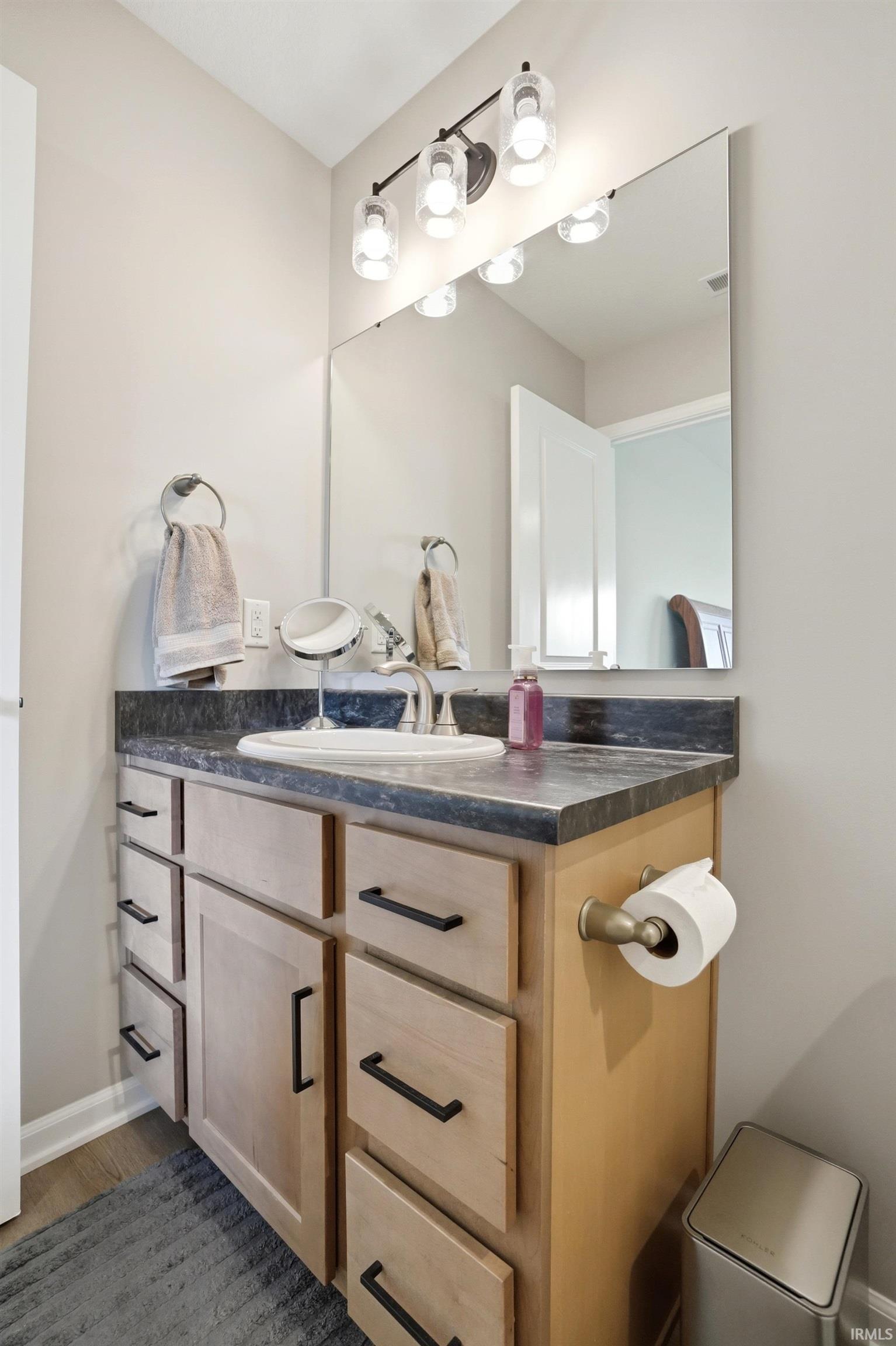Light wood-finish vanity with black hardware, dark countertop, and integrated sink