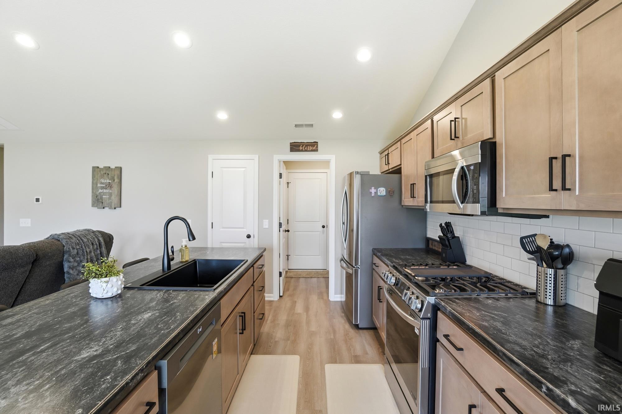 Kitchen featuring wood-finish flooring, dark countertops, and light wood cabinetry with black hardware