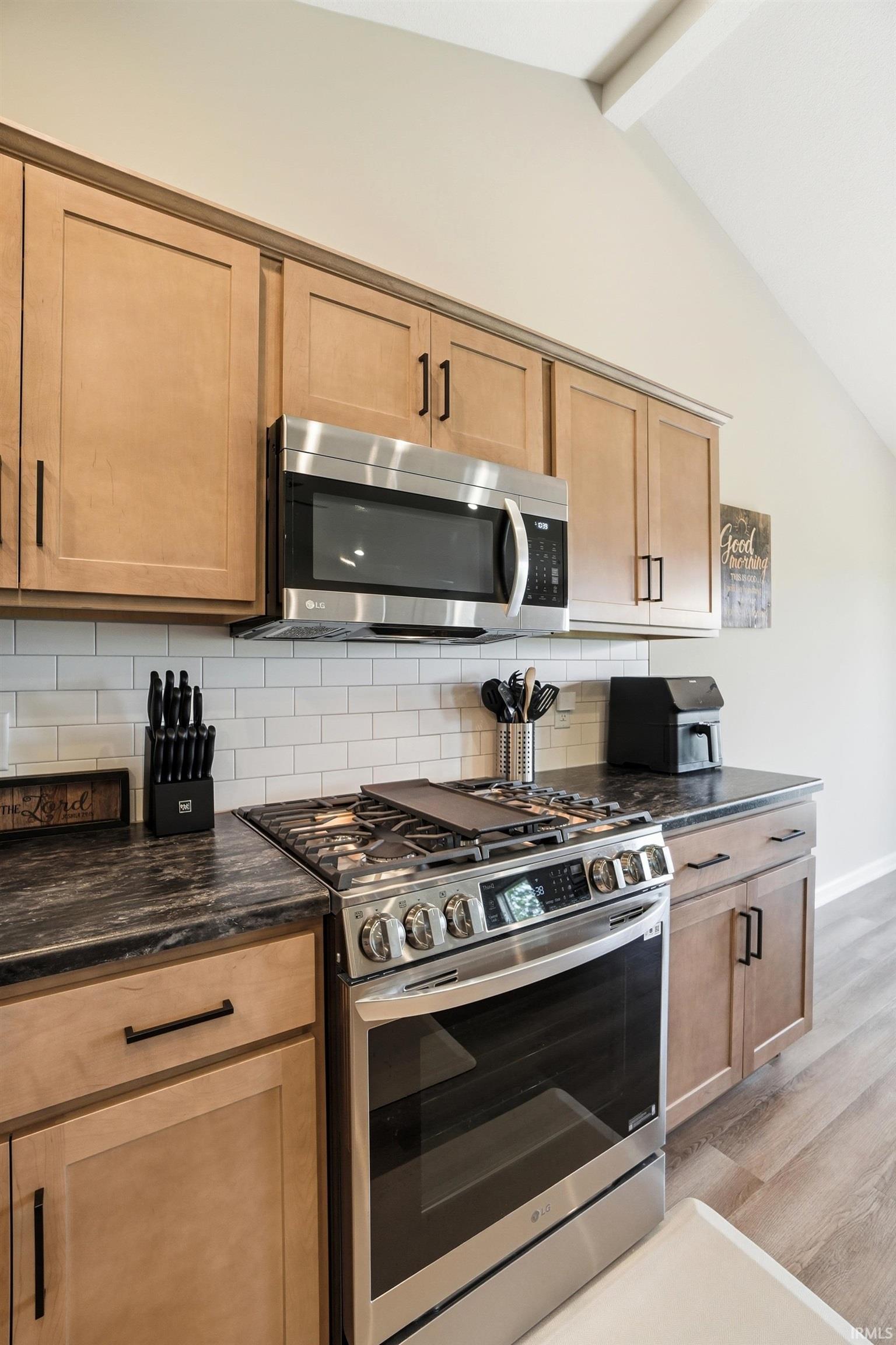 Kitchen featuring stainless steel range with griddle, stainless steel microwave, light wood-finish cabinetry with black pulls, dark countertops, and white subway tile backsplash