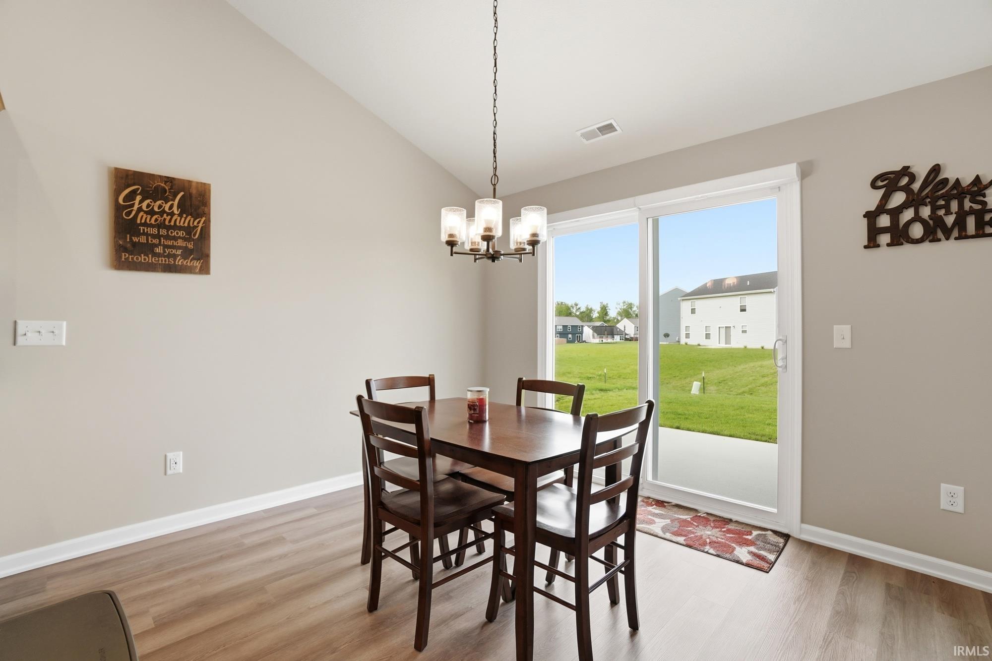 Dining area featuring wood-finish flooring, a vaulted ceiling, and a contemporary chandelier