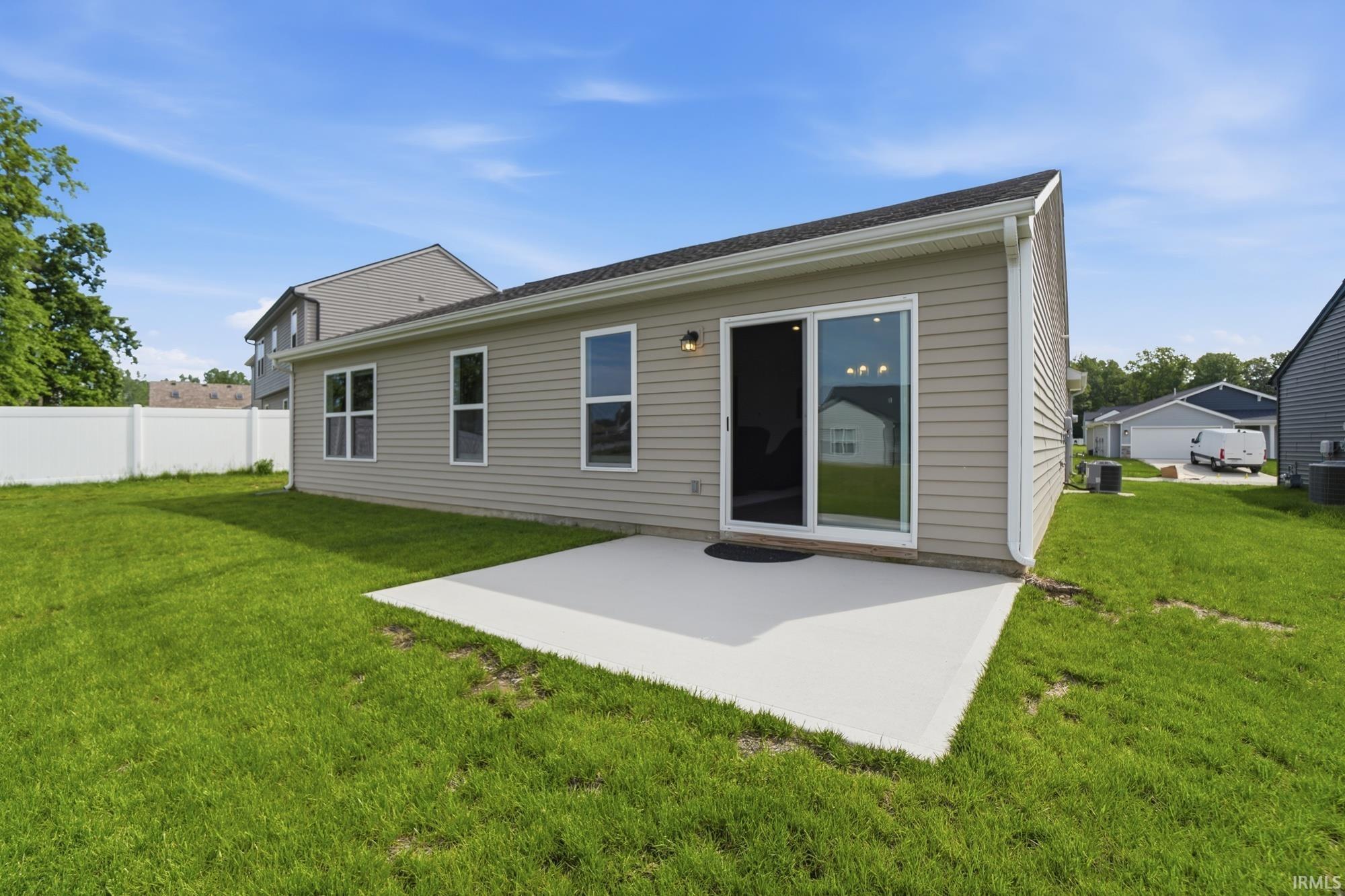Rear exterior with tan horizontal siding, featuring a concrete patio and a large sliding glass door