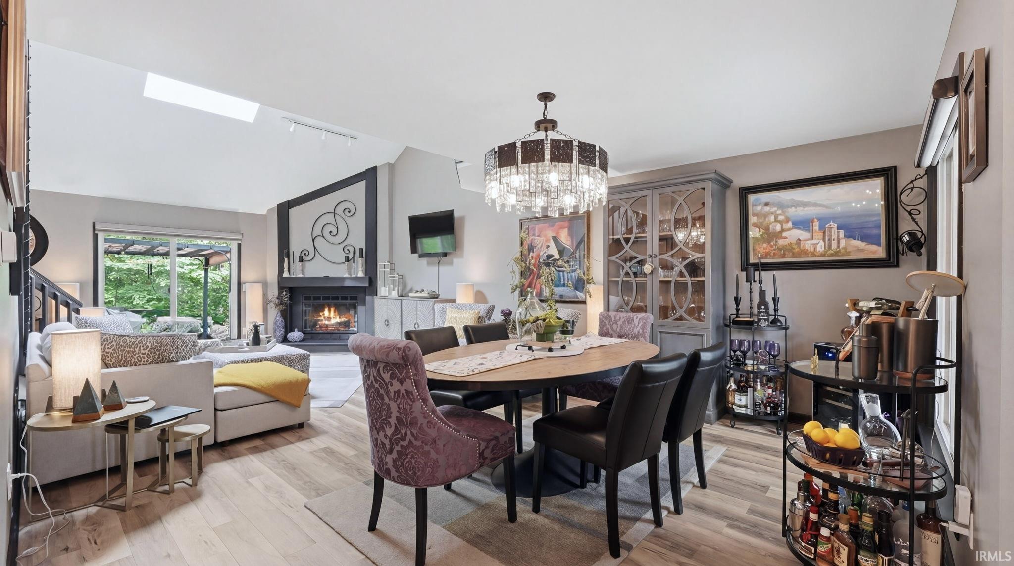 Open-concept living area featuring wood-finish flooring, a vaulted ceiling with a skylight, and a built-in fireplace with a decorative mantel