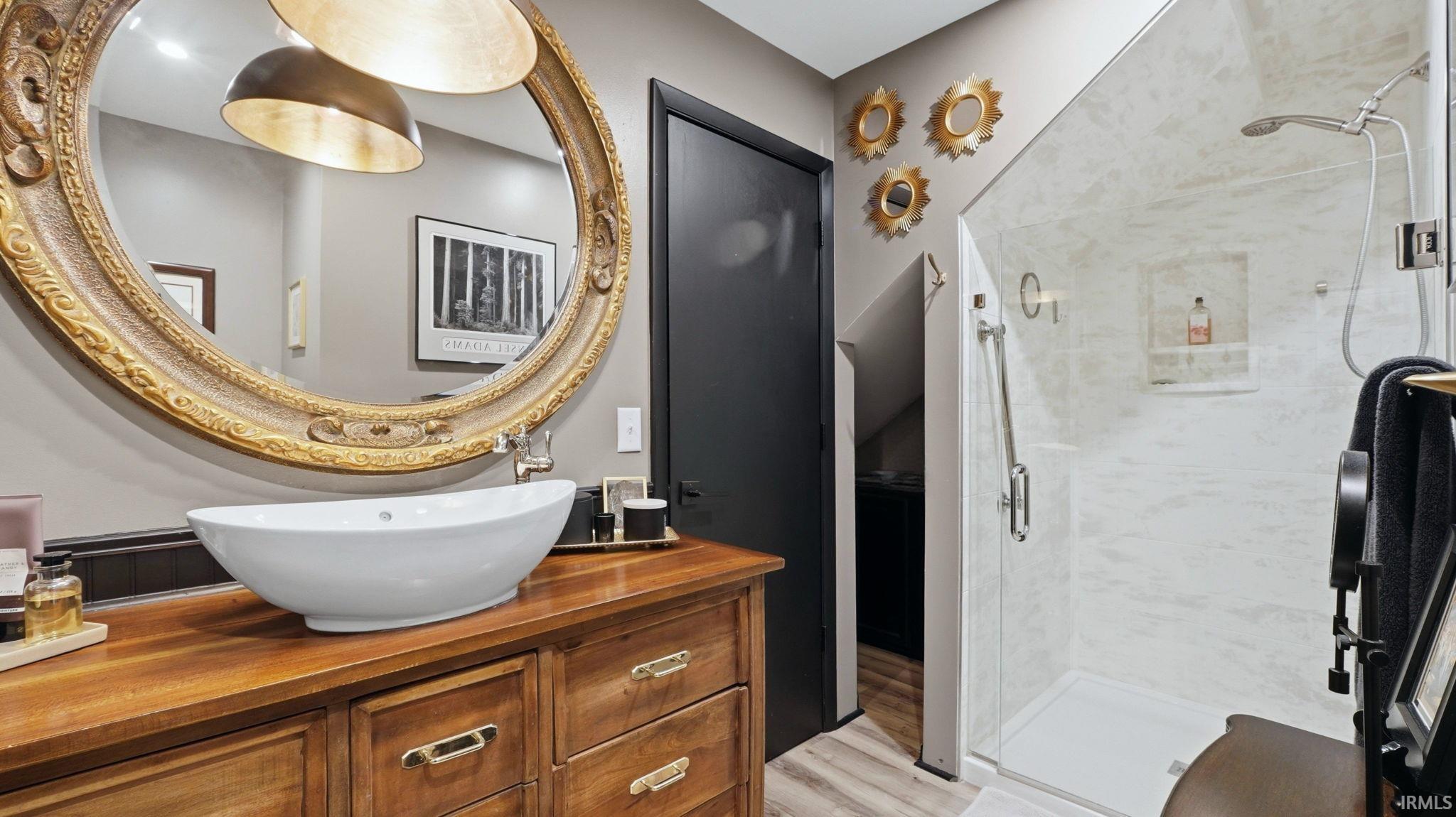 Bathroom featuring a vessel sink on a wood-finish vanity, ornate gold-tone framed mirror, and a glass-enclosed shower with white tiled walls and built-in niche