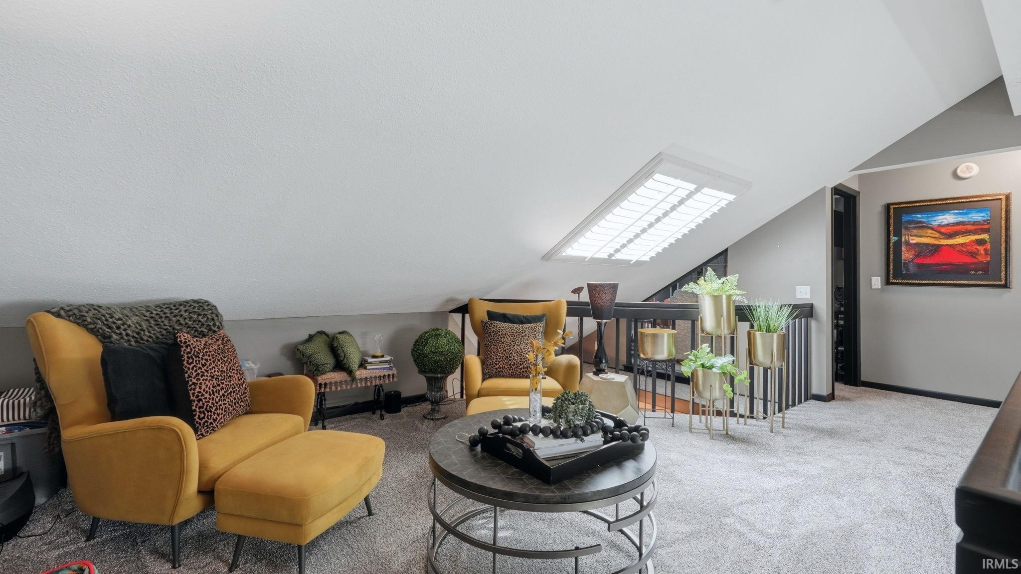 Carpeted loft area featuring a sloped ceiling with an integrated skylight, dark wood railing, and neutral wall tones