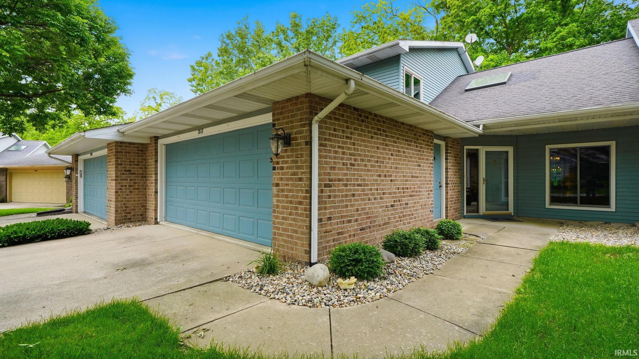 Brick and siding exterior featuring two light blue garage doors, a concrete driveway, and a concrete walkway