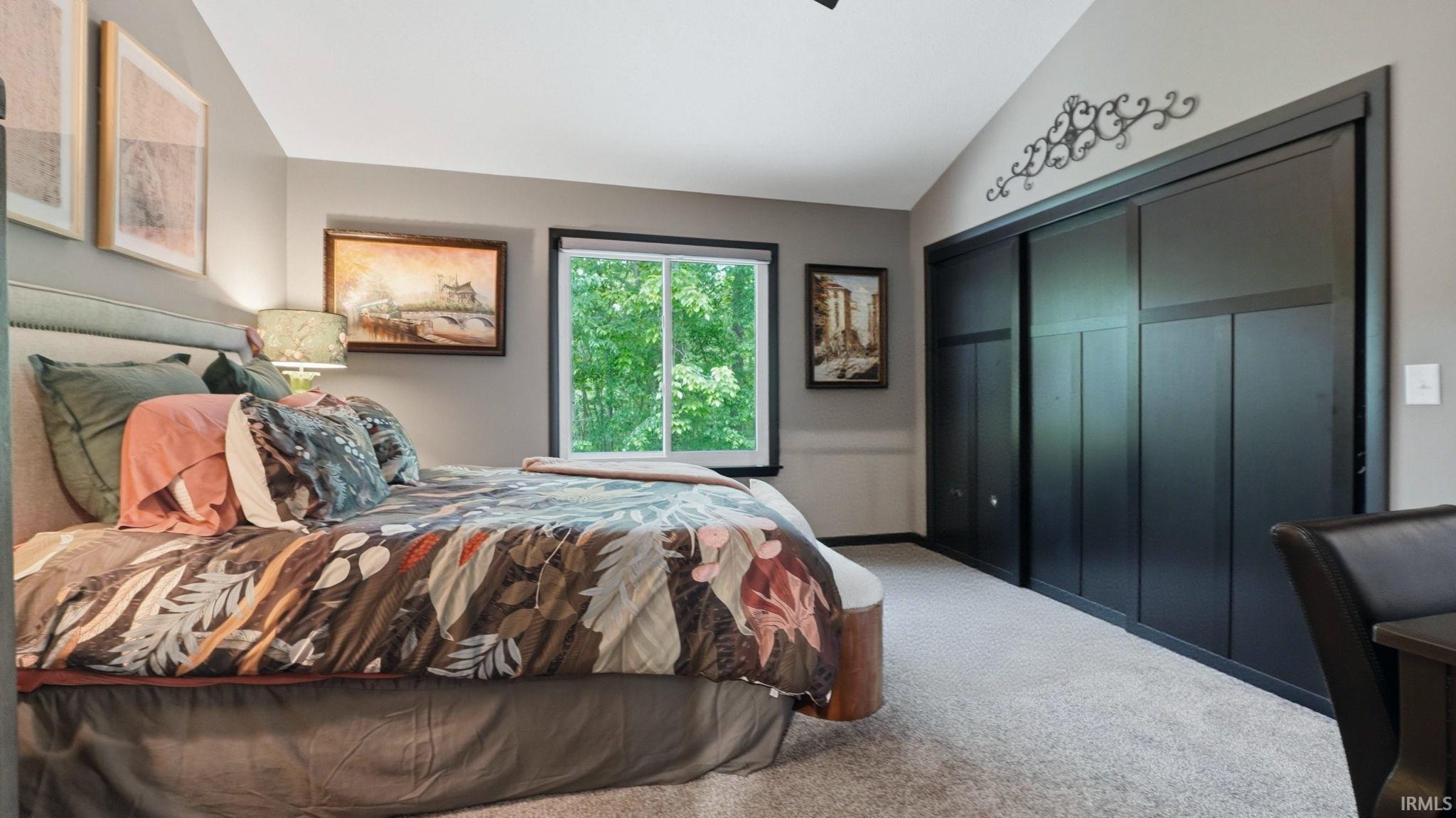 Bedroom featuring a vaulted ceiling and a window with green foliage scenery