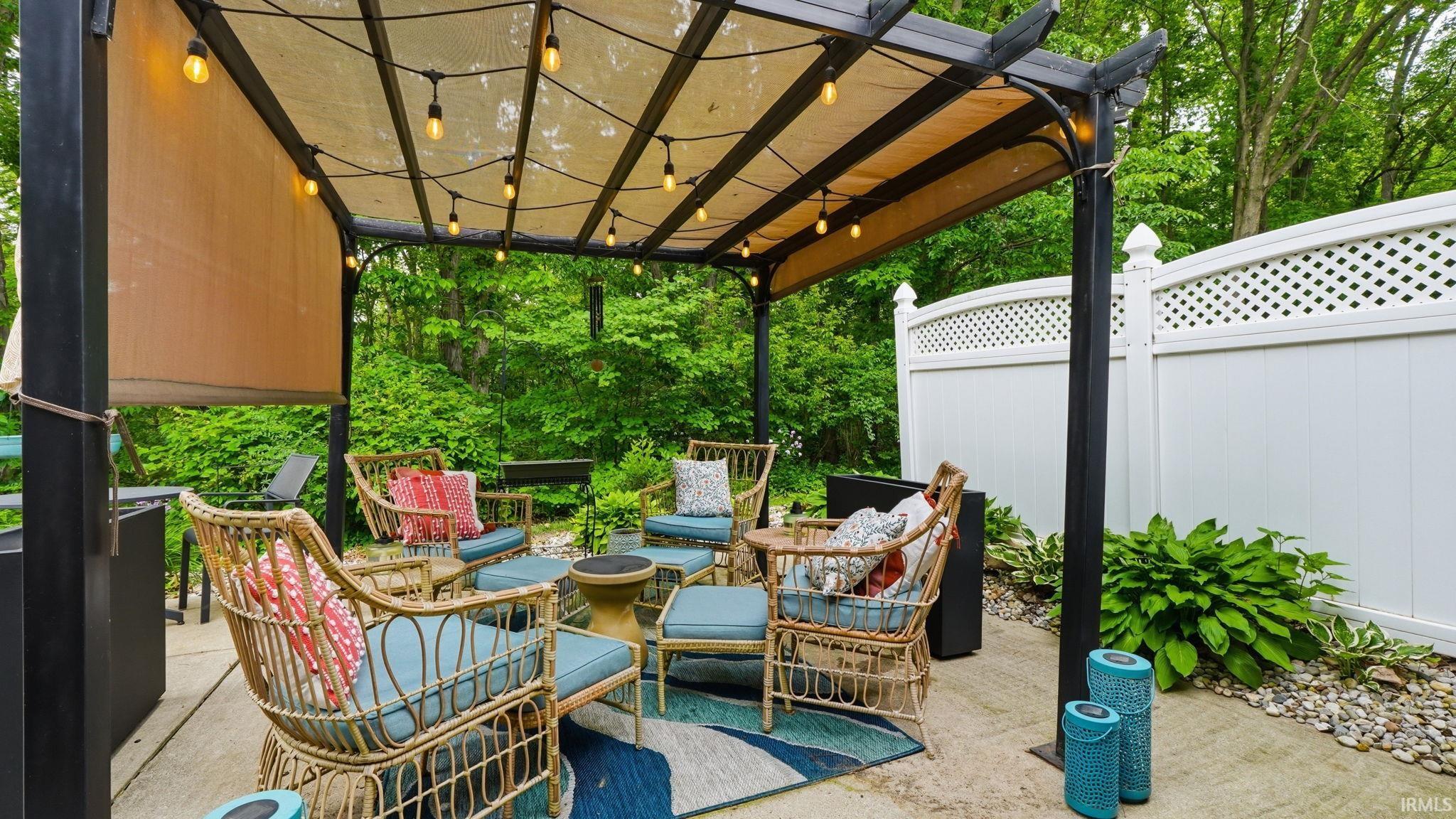 Outdoor patio featuring a black metal pergola with a light-colored fabric canopy and string lighting