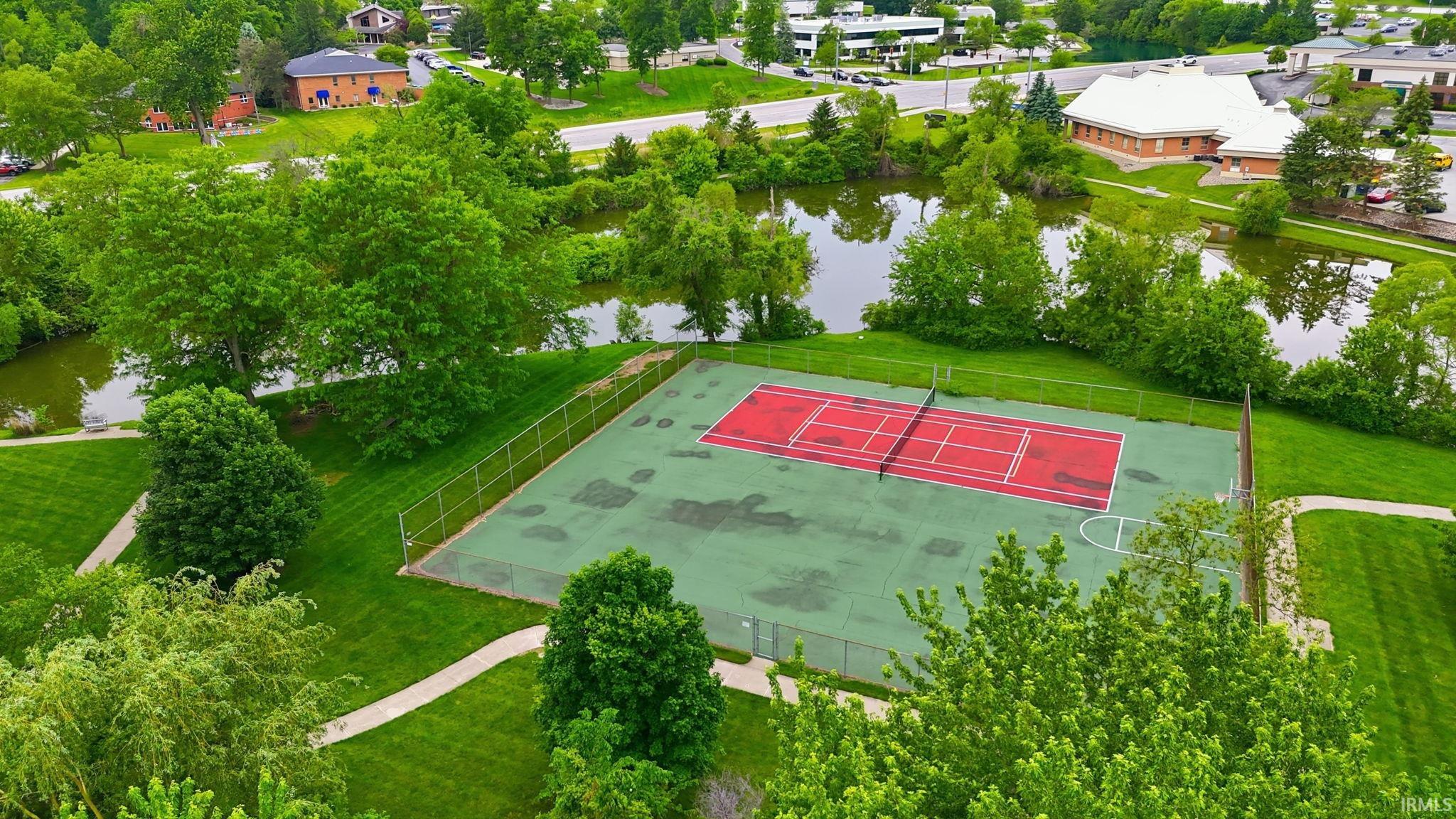 Outdoor tennis court with a green surface and red playing area, featuring a white net